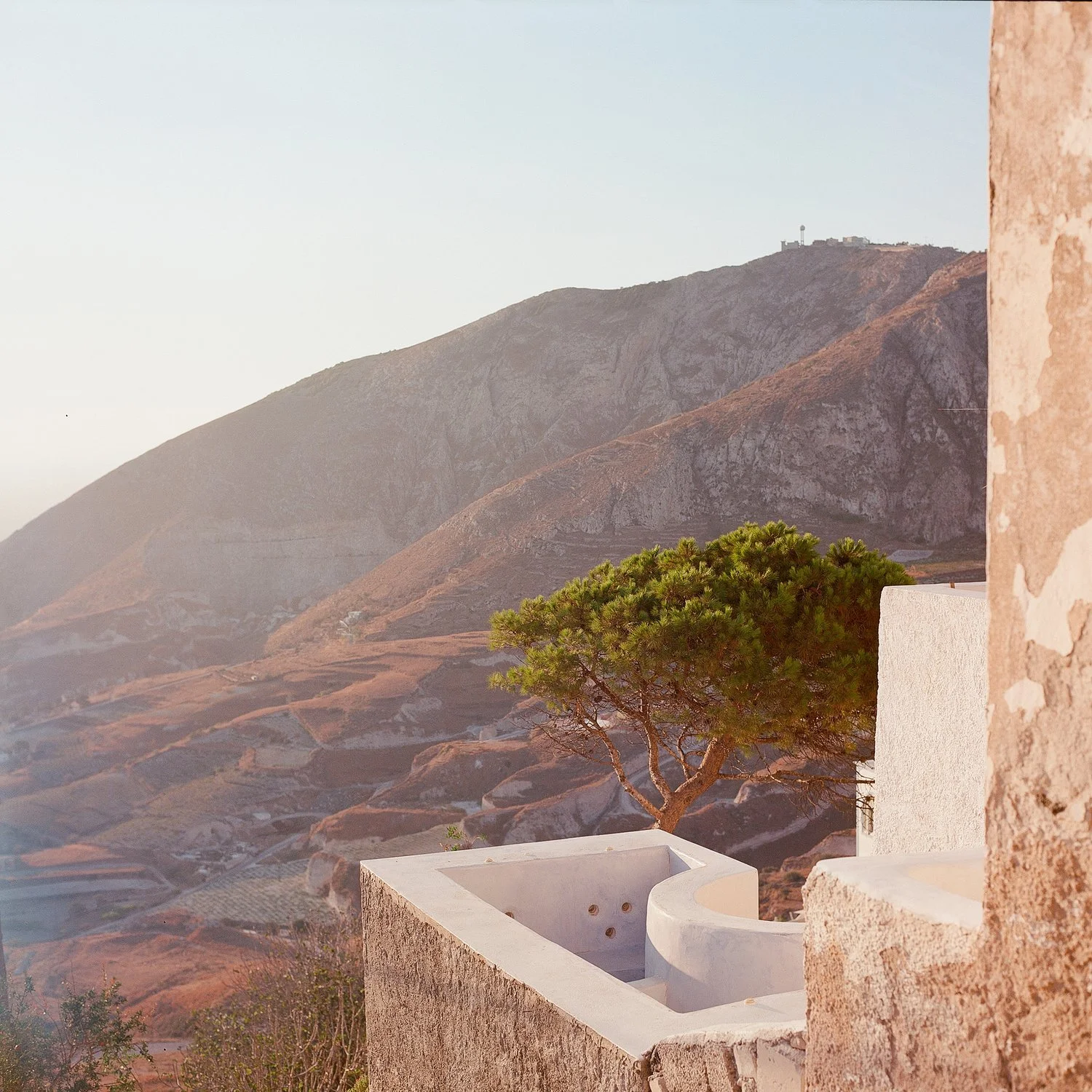 A scenic view of rugged mountains with a white building and a green tree in the foreground.