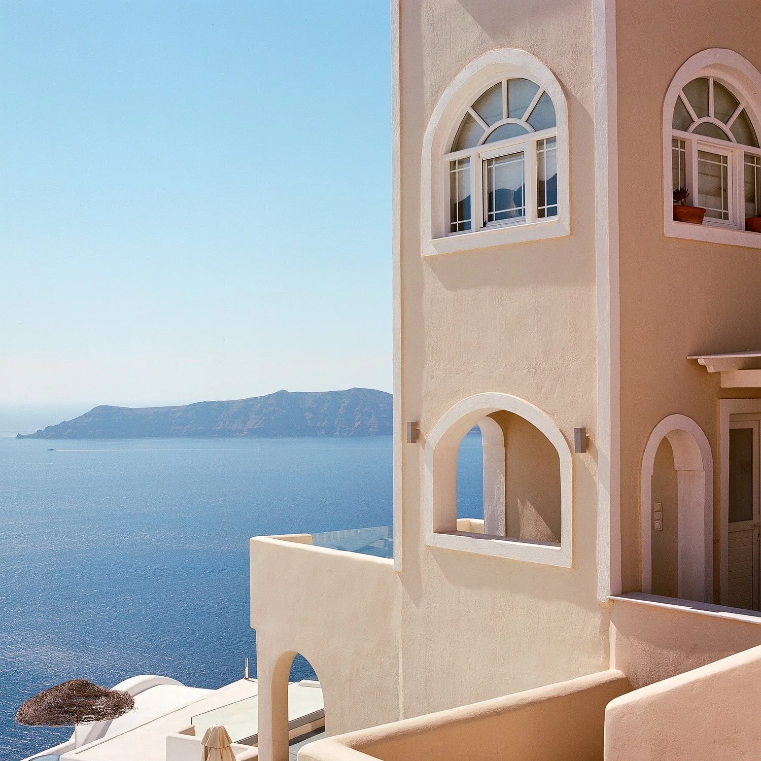 A building with arched windows and a balcony overlooks the ocean and a mountainous island in the background.