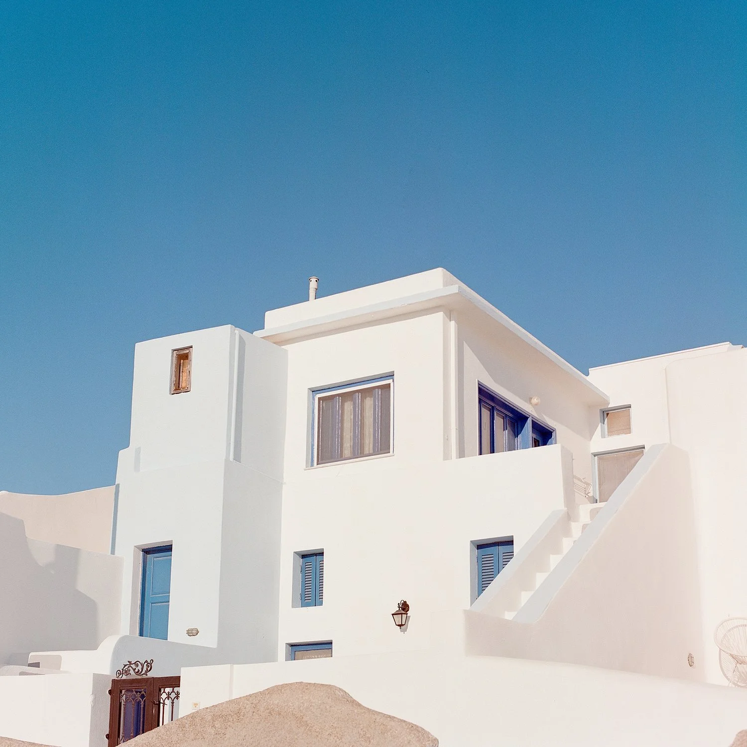 White modern multi-story building with blue windows, stairs, and a black lantern against a clear blue sky.