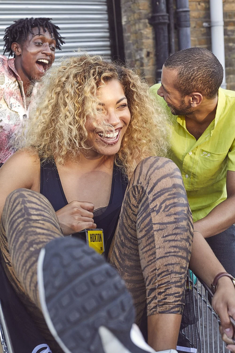 A group of four friends laughing and enjoying each other's company outdoors, with a woman sitting in a stroller and wearing leopard print leggings, and others standing behind her, all smiling and sharing a joyful moment.
