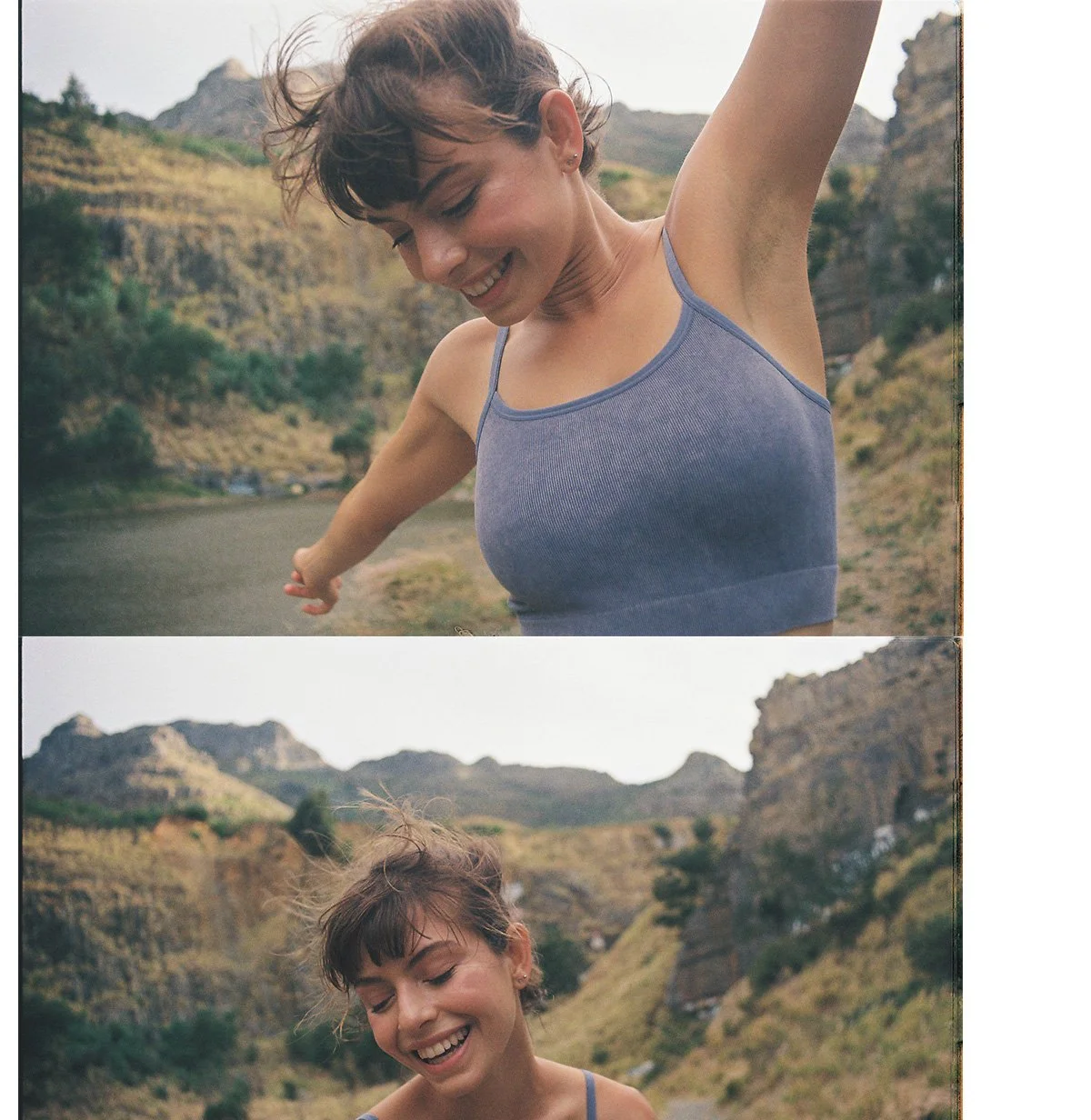 A young woman with short brown hair smiling and enjoying nature in a mountainous outdoor setting, wearing a blue tank top.