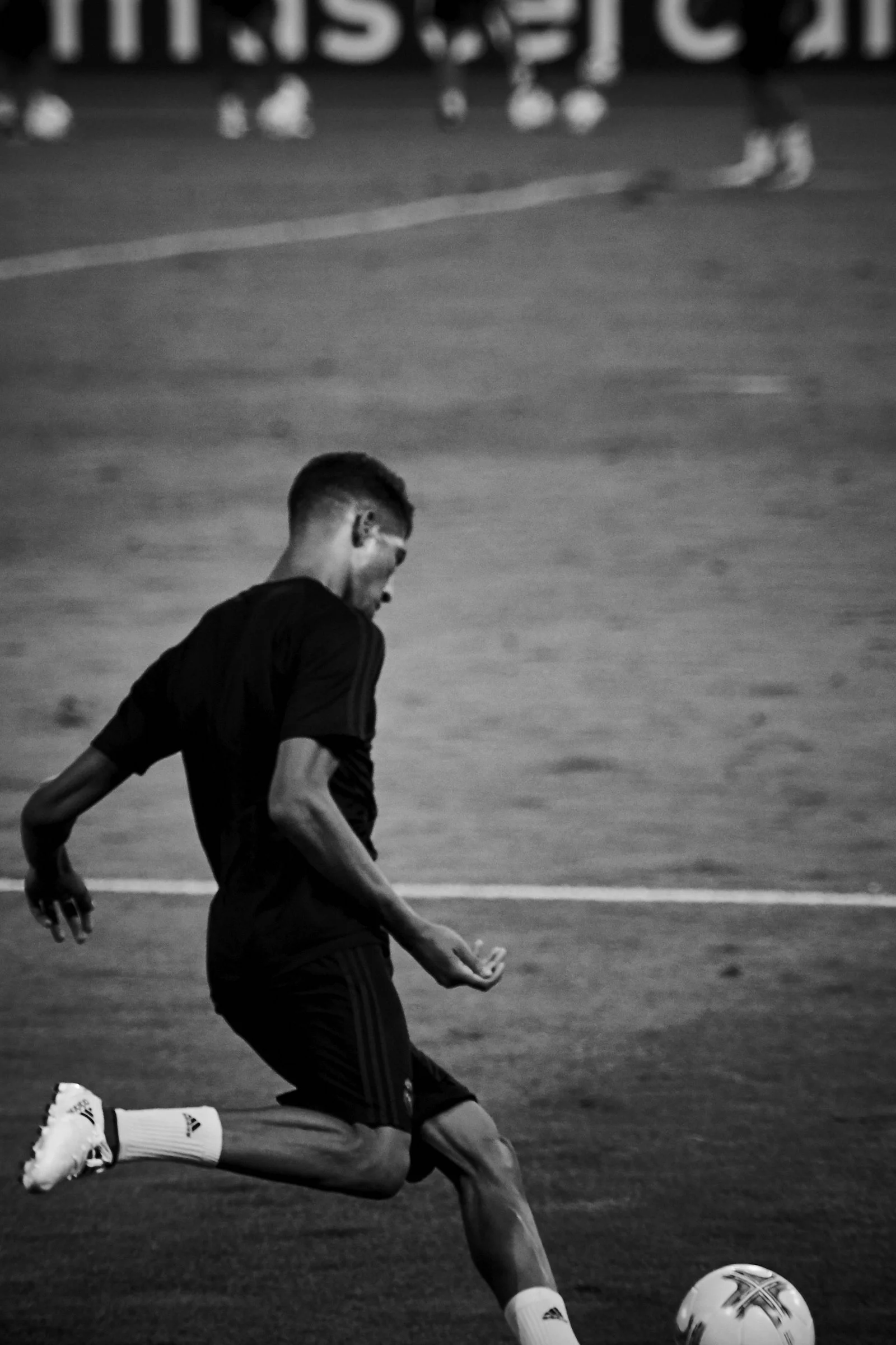 A young male soccer player in black uniform1, wearing white Adidas cleats and socks, is kicking a soccer ball on the field.