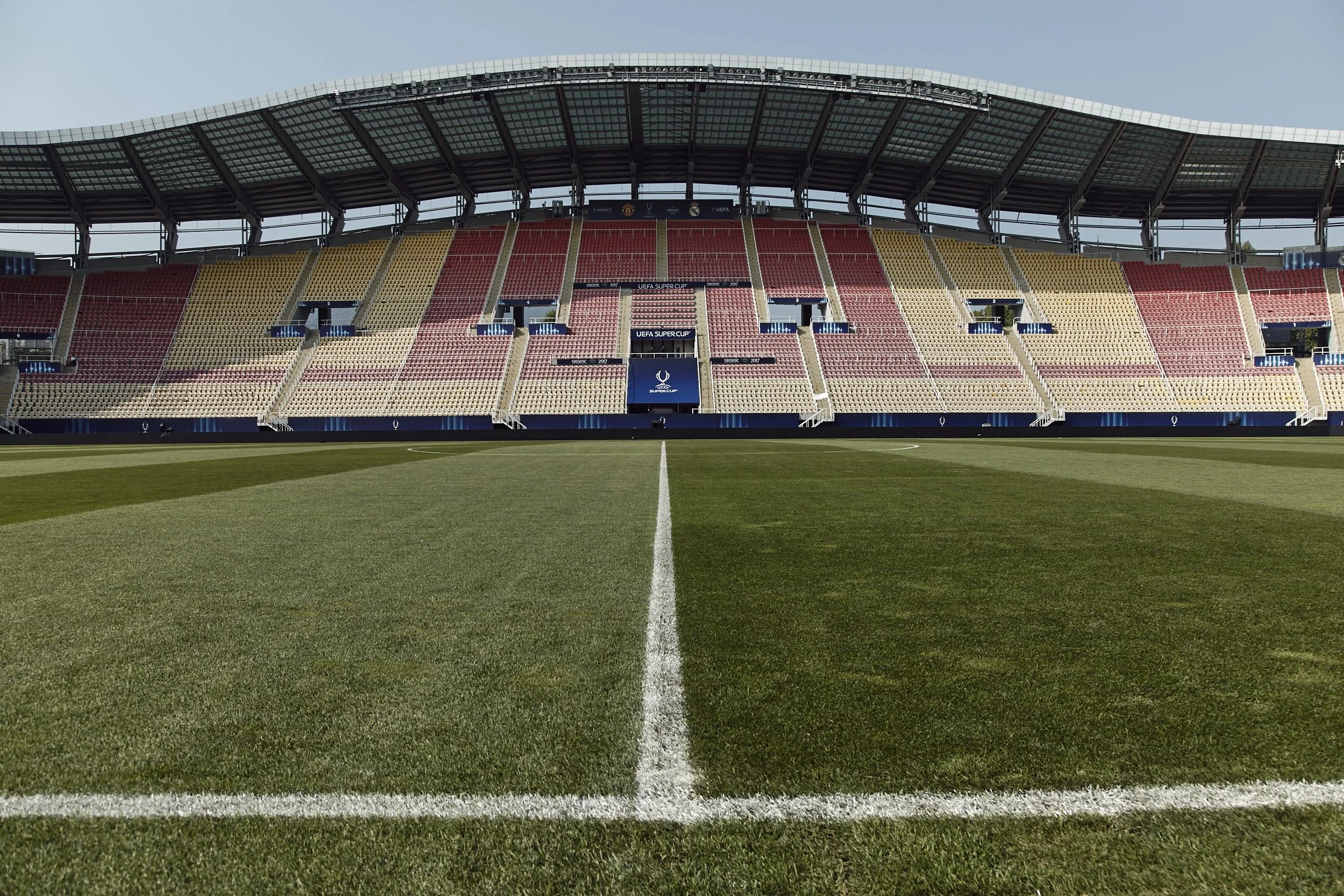 Empty soccer stadium with a green field and colorful seats, view from midfield.