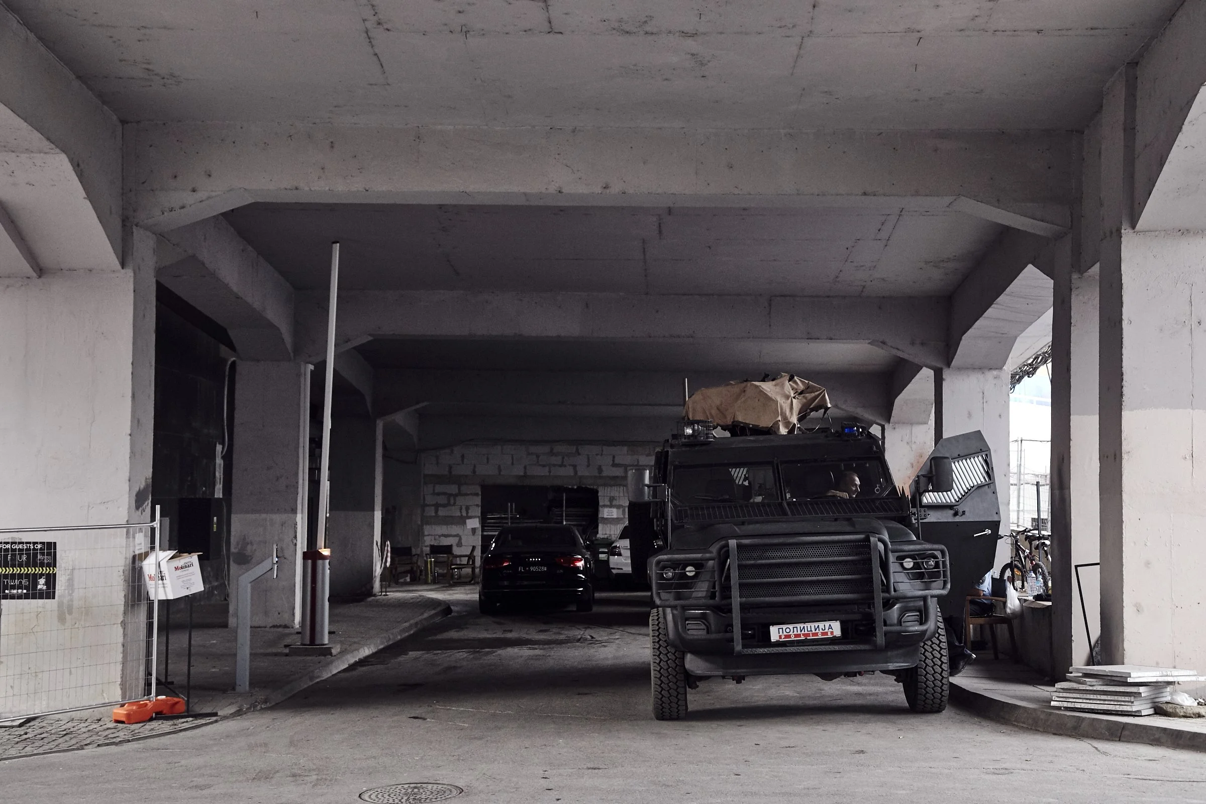 Underpass with police vehicle and black car parked underneath, construction materials on side, and bicycle on the side, with no visible people.