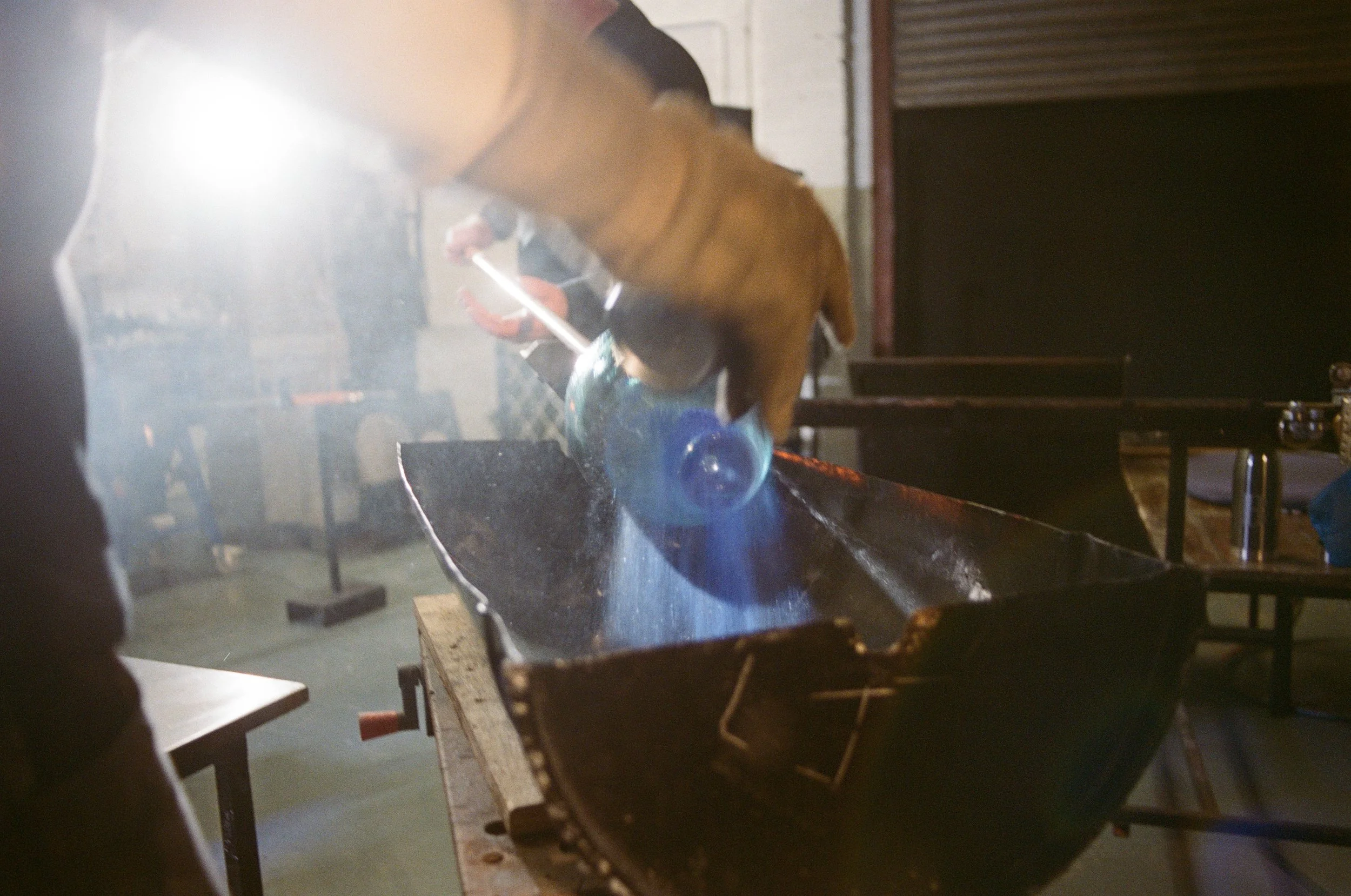 A person is blowing glass into a molten piece in a glassblowing studio.