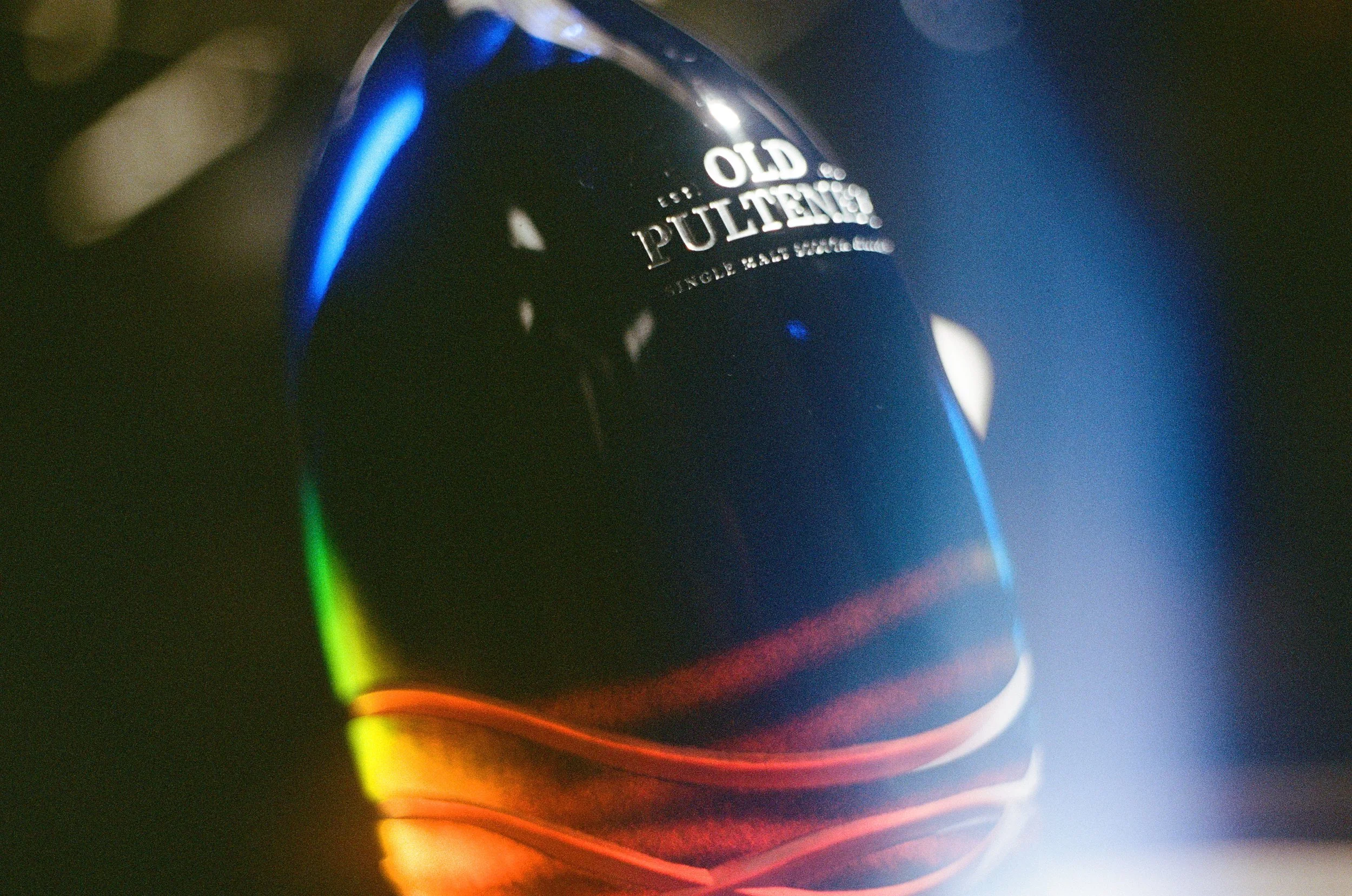 A dark bottle of Old Pulley whiskey with colorful rainbow reflections on its surface.