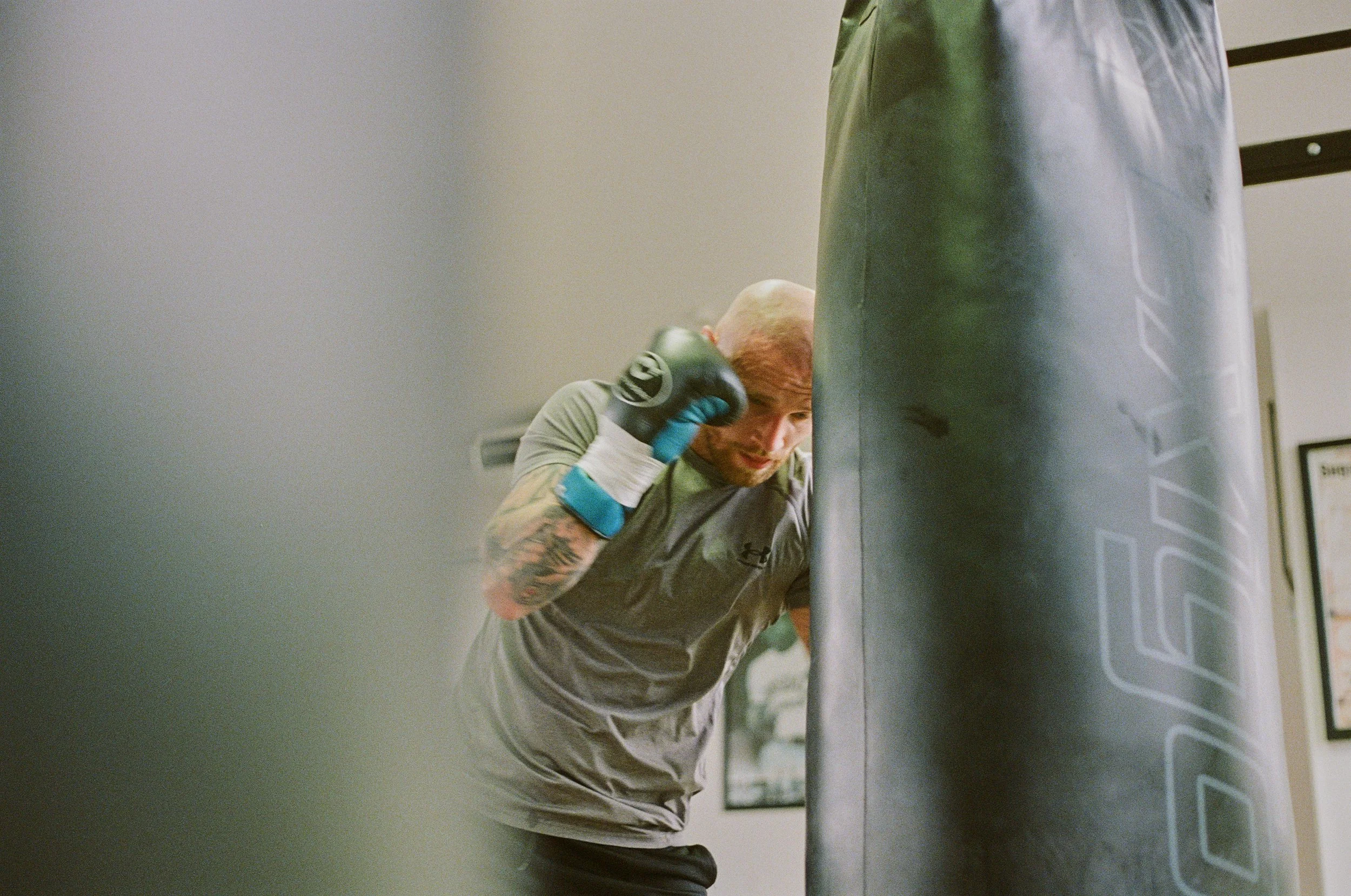 A man with tattoos on his arm throwing a punch at a punching bag in a gym.
