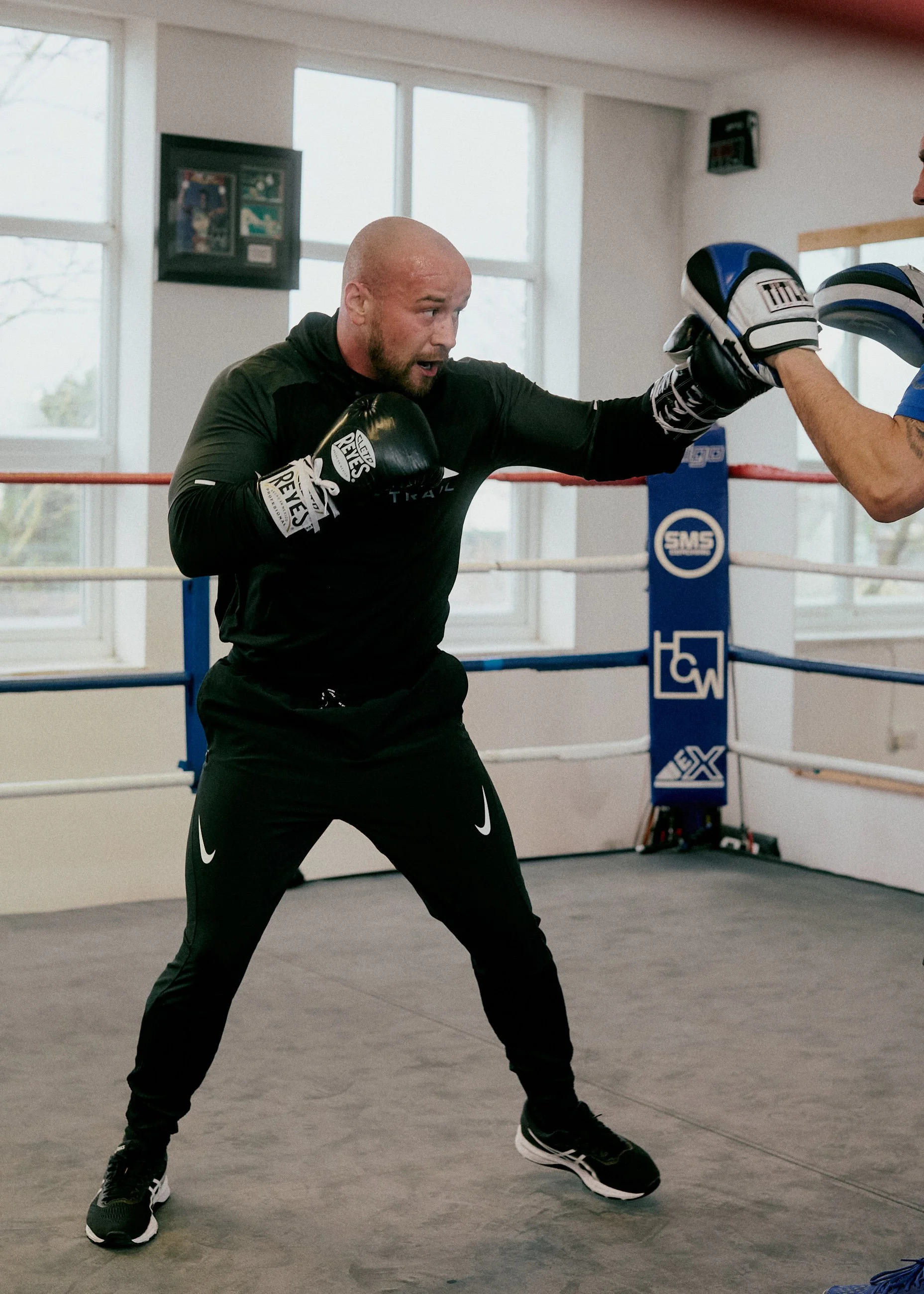 A man practicing boxing in a gym, wearing gloves and throwing a punch towards a partner or trainer.