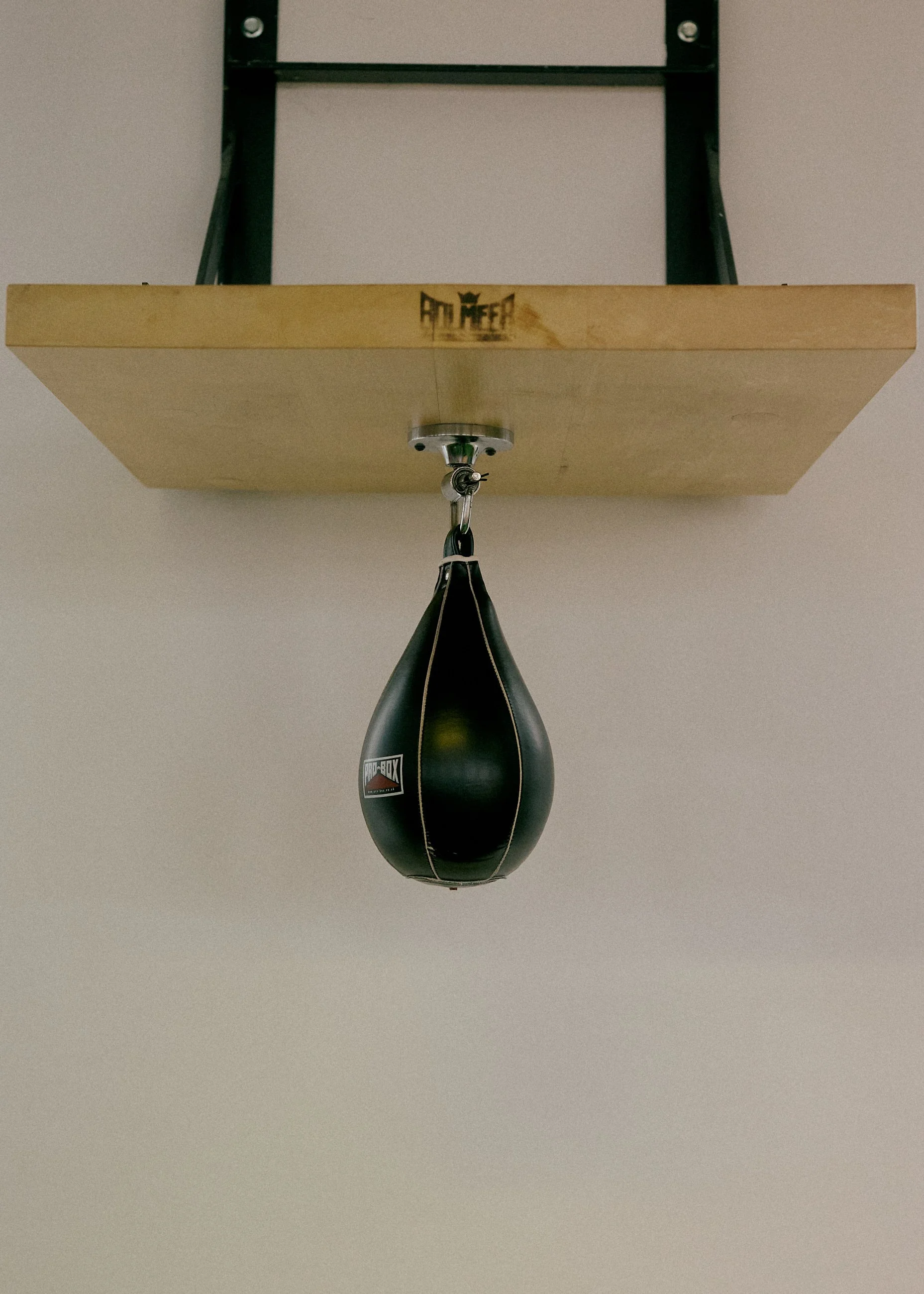 A black speed bag hanging from a metal platform in a gym or boxing training area.
