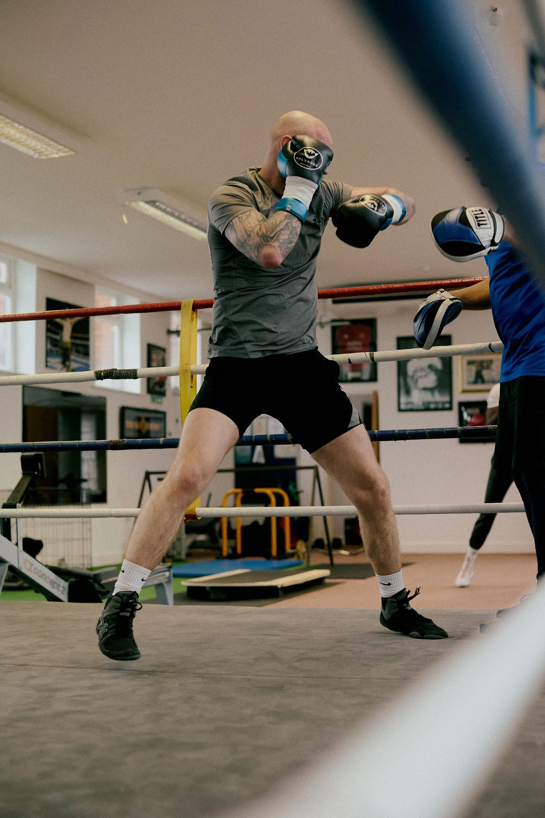 A boxer practicing in a boxing gym, wearing gloves and shorts, standing in a fighting stance inside a boxing ring.