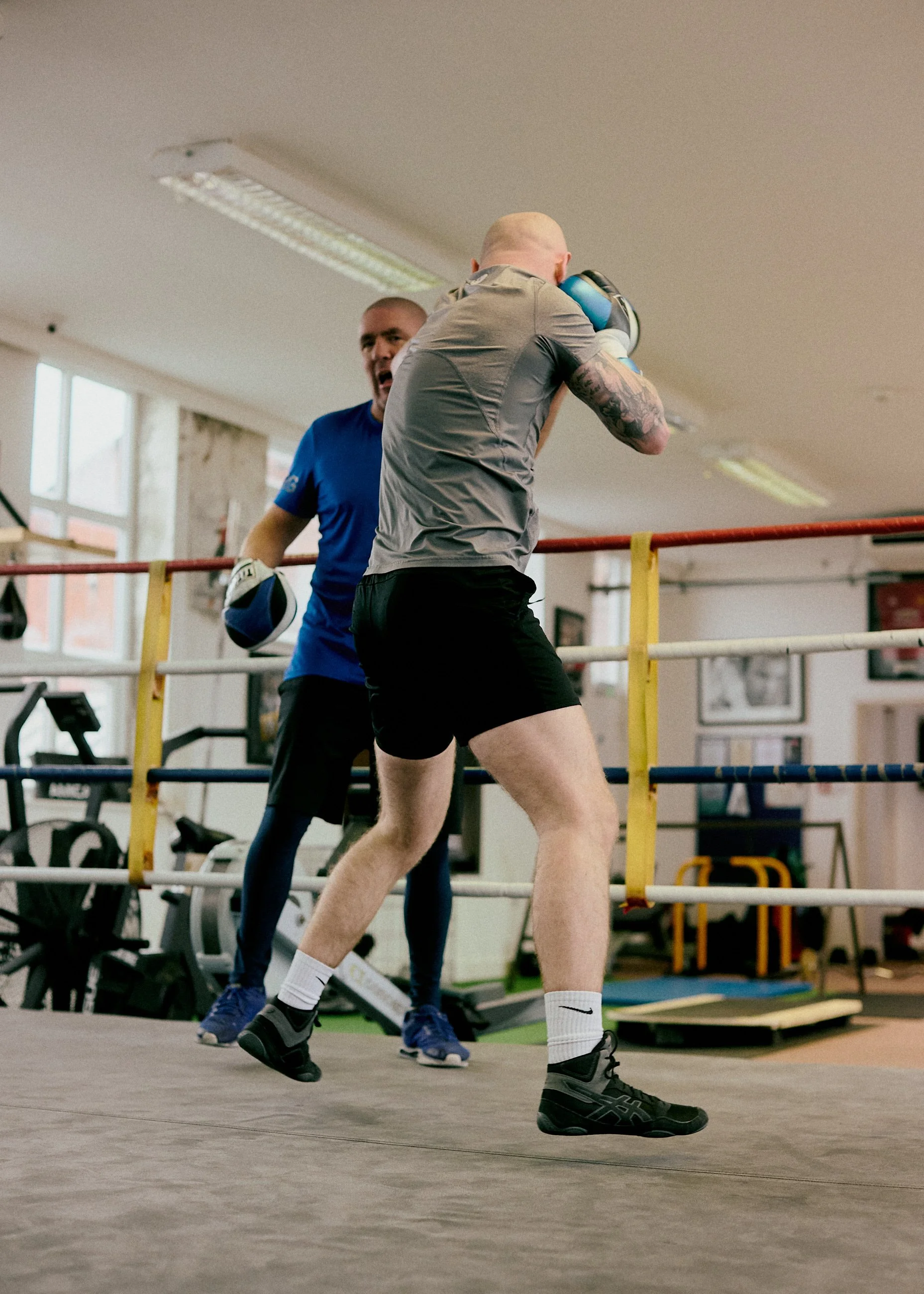 Two men boxing inside a gym, one actively throwing a punch and the other blocking with gloves.