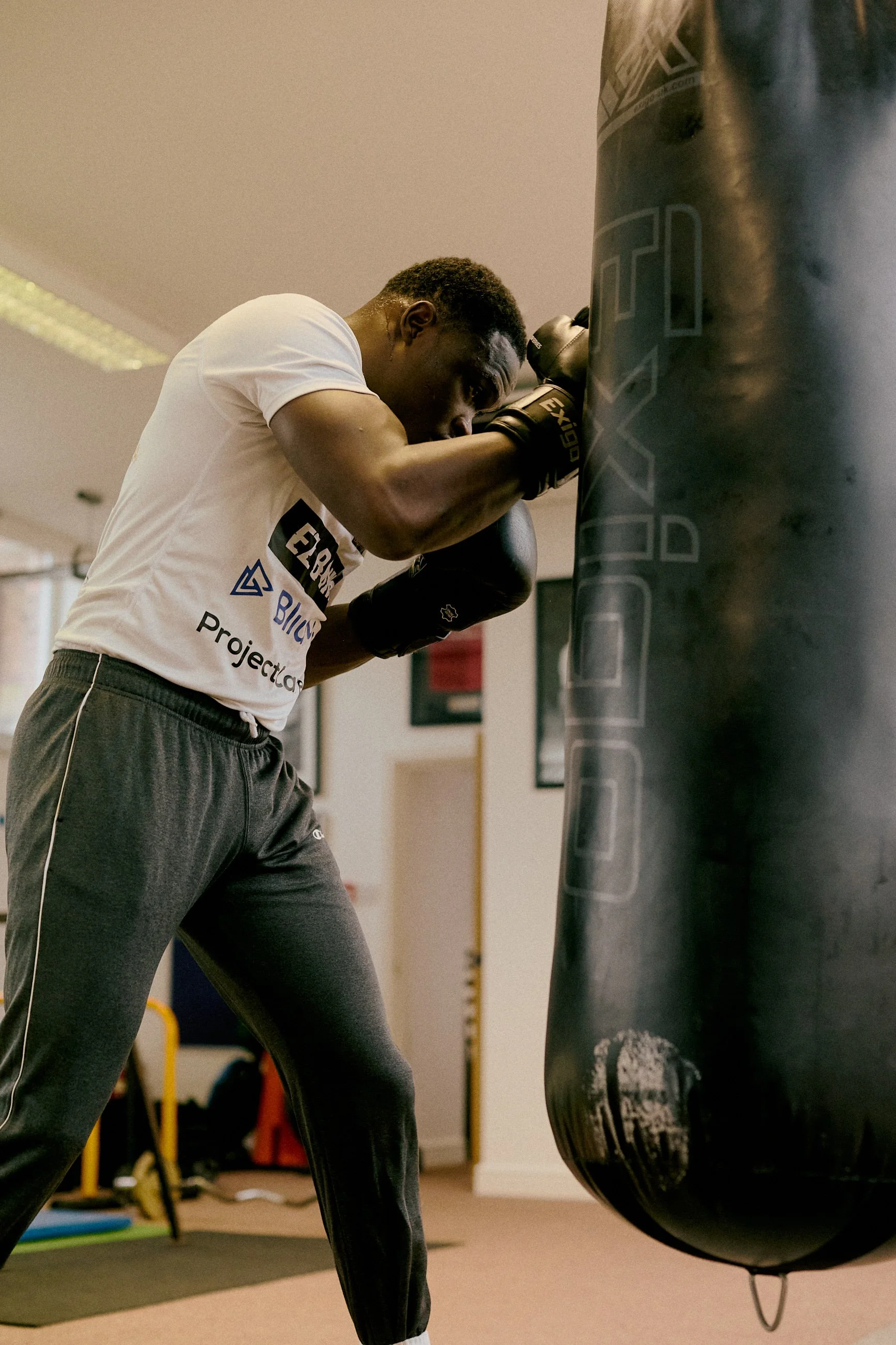 A young man practicing boxing by punching a hanging black punching bag in a gym.