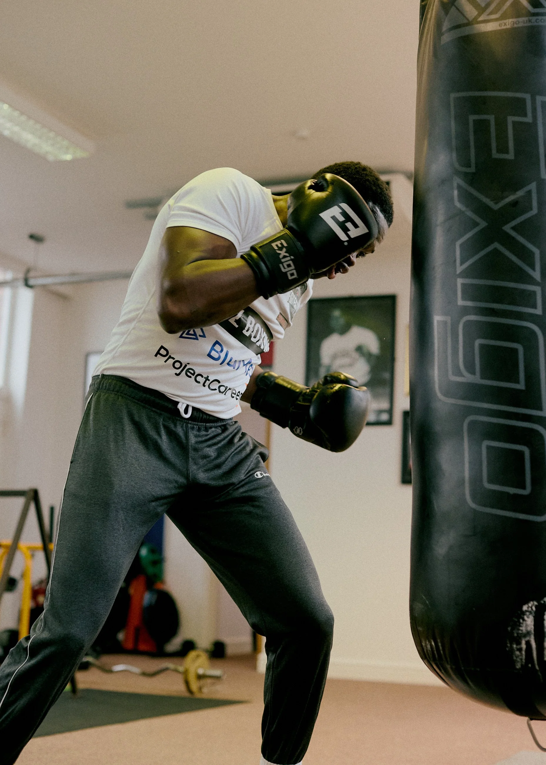 A man wearing black boxing gloves practicing punches on a punching bag in a gym.