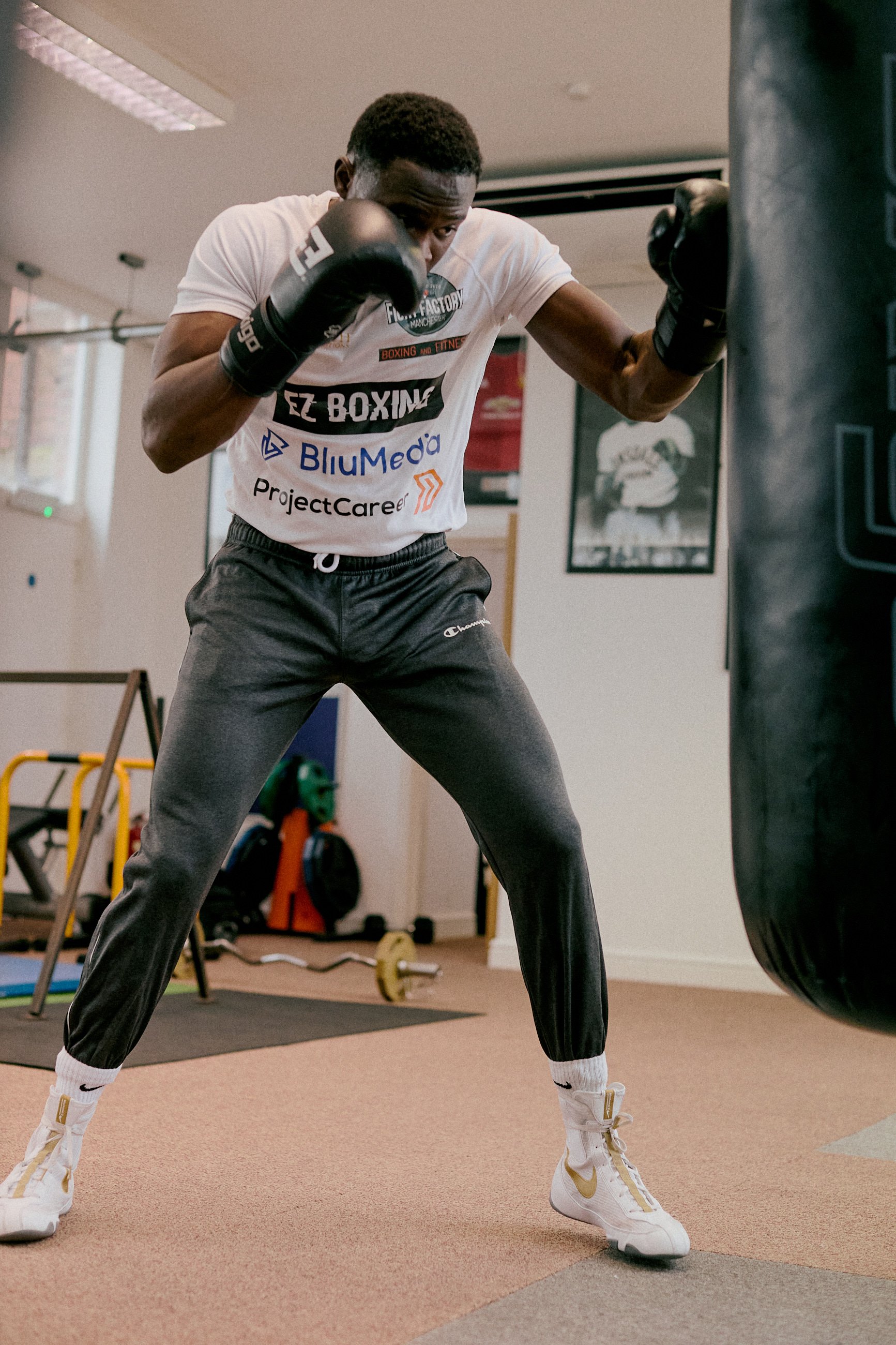 A young man training with boxing gloves in a gym, punching a heavy bag.