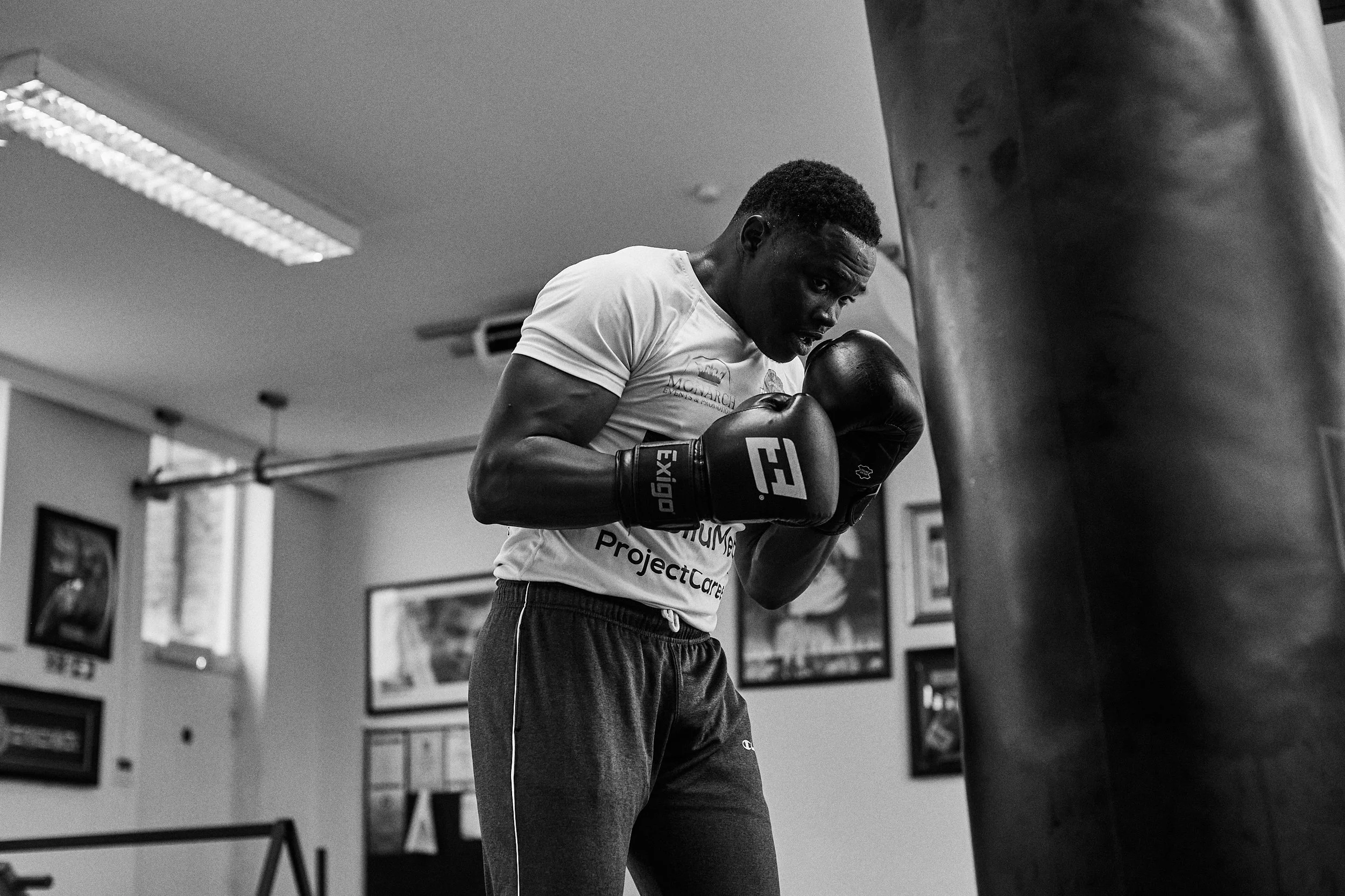 A man in a gym wearing boxing gloves, practicing boxing on a punching bag.