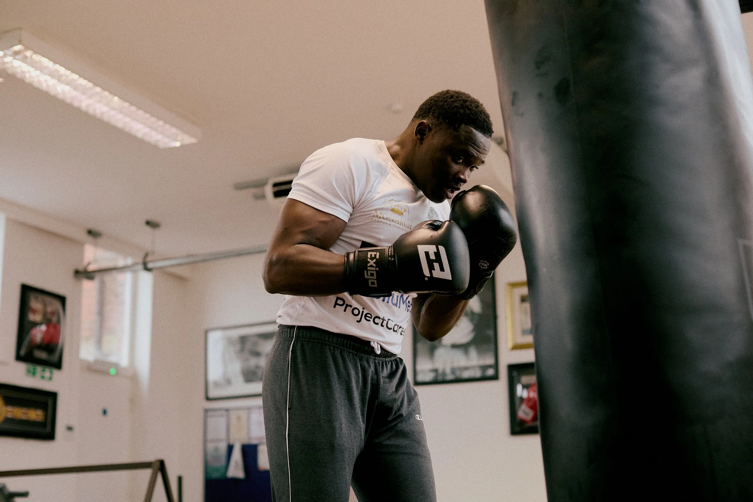 Man in a white t-shirt and gray sweatpants punching a black punching bag in a gym.