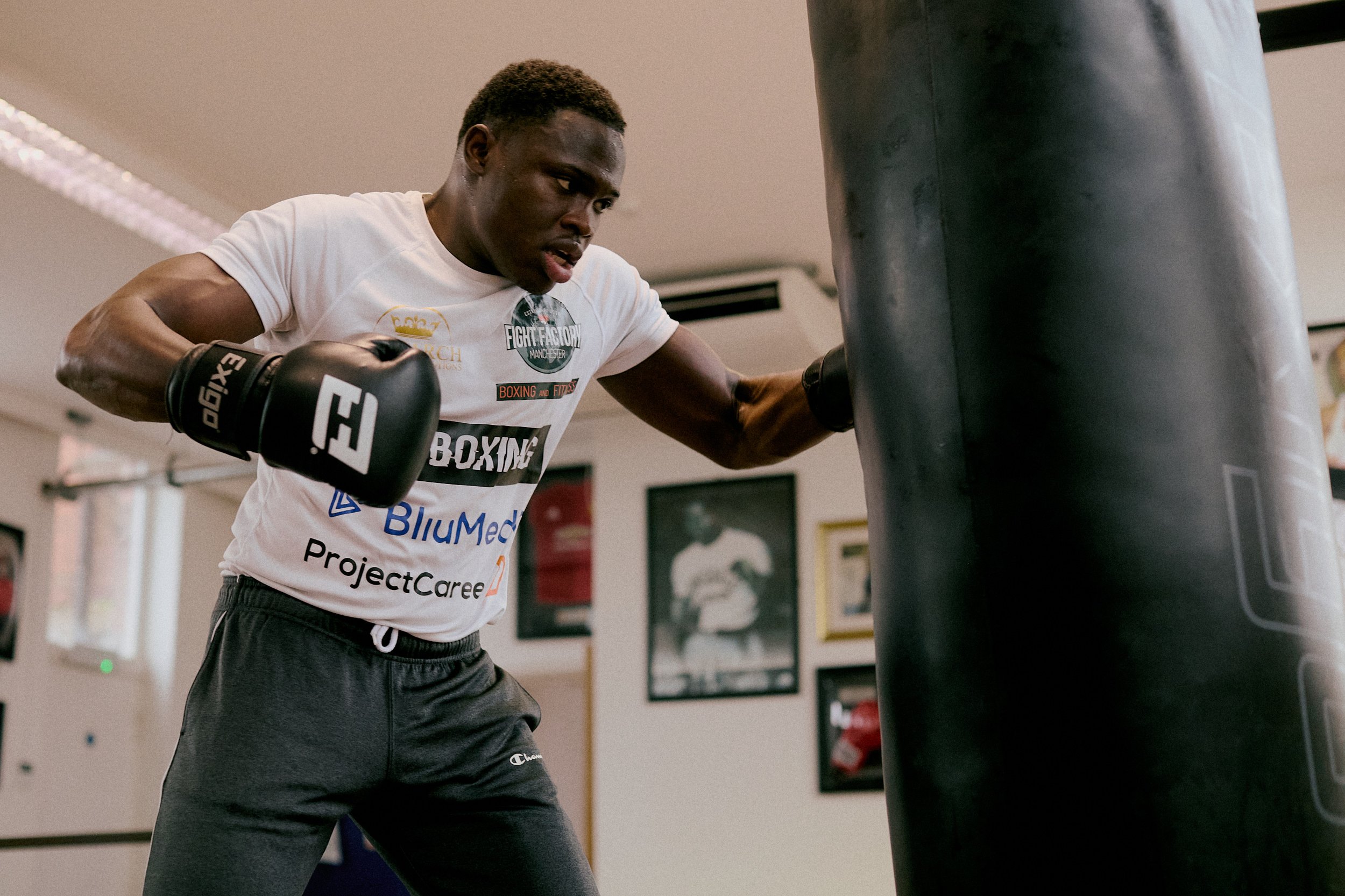A young man training with a punching bag in a gym, wearing boxing gloves and a T-shirt.