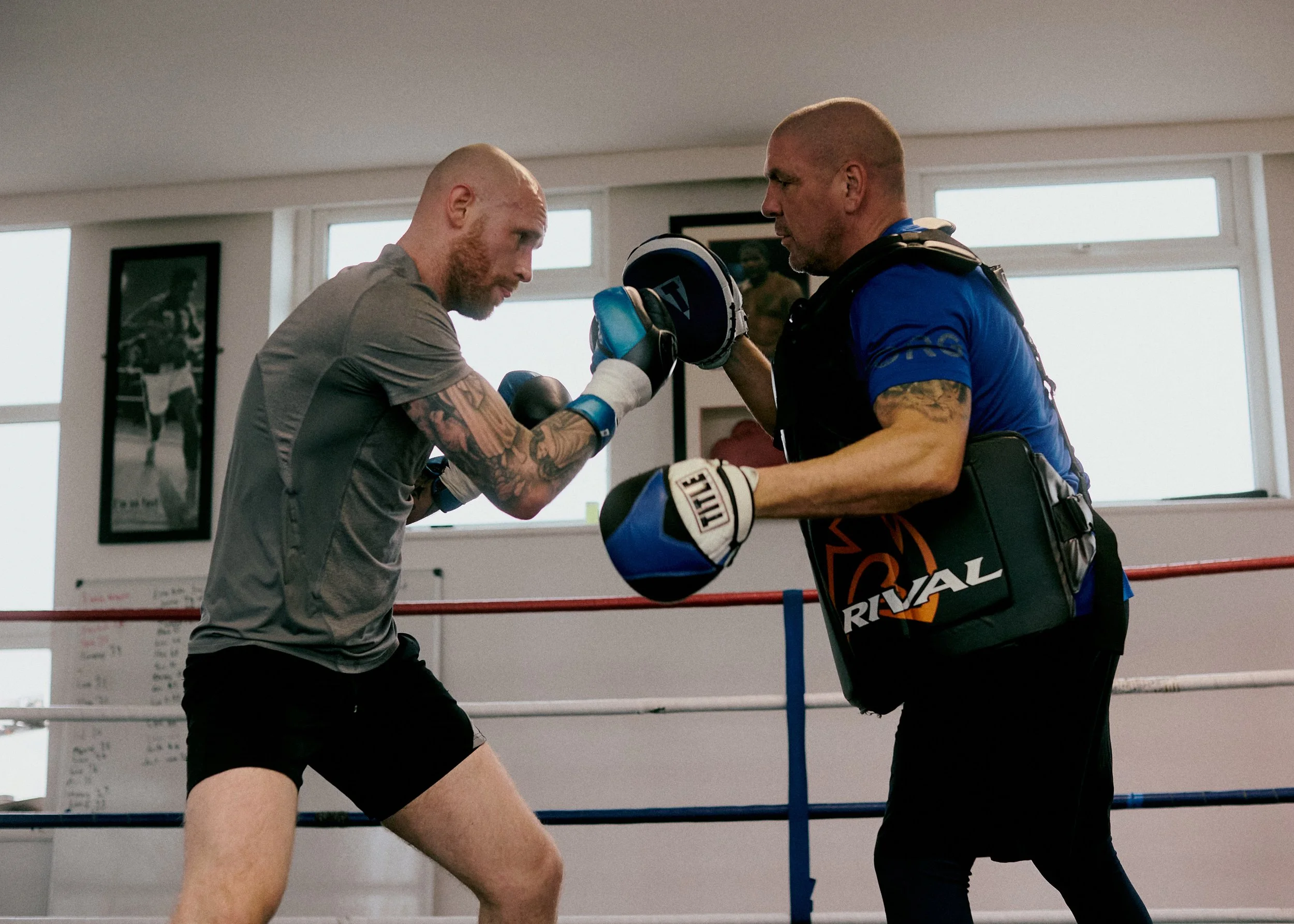 Two men practicing boxing in a gym, with one man throwing a punch and the other man holding boxing pads.