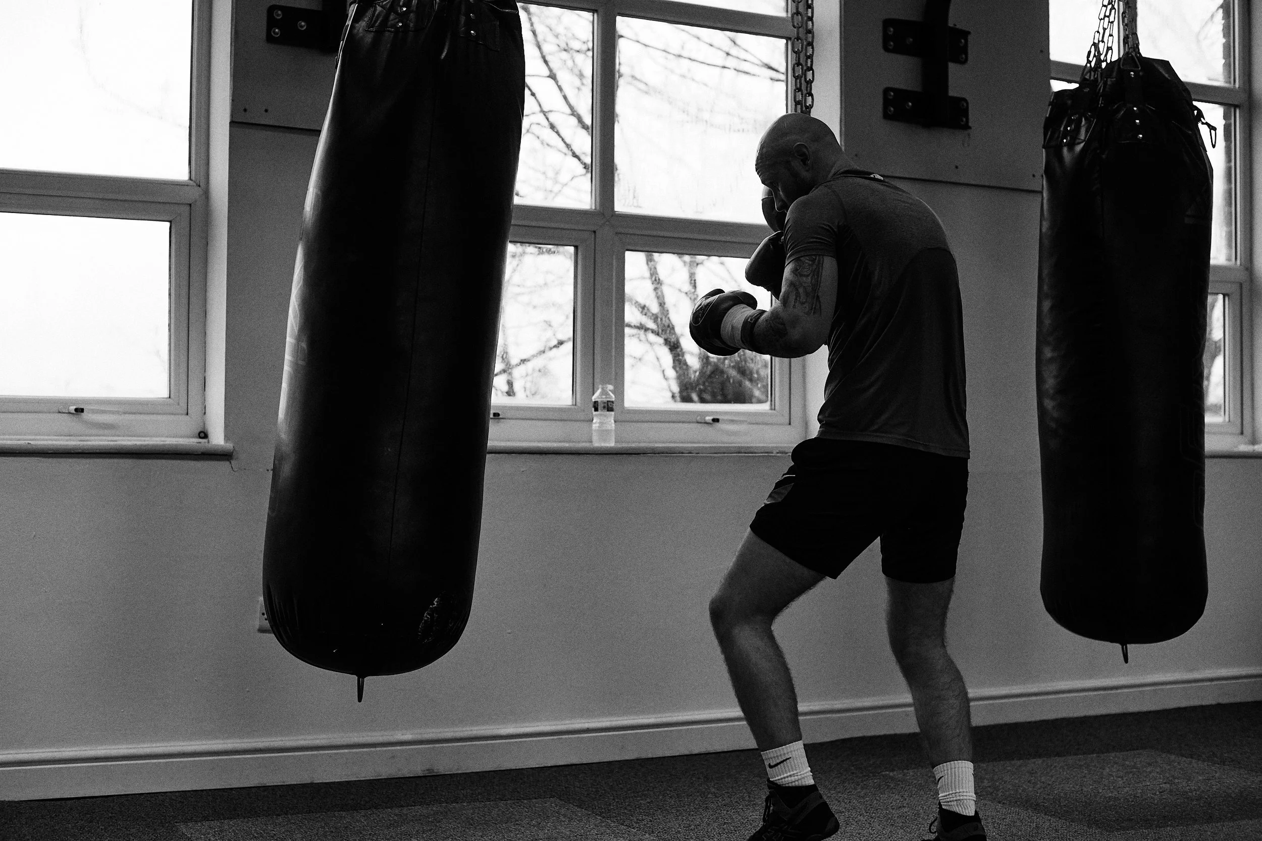A man practicing boxing in a gym, standing in front of punching bags and wearing gloves.