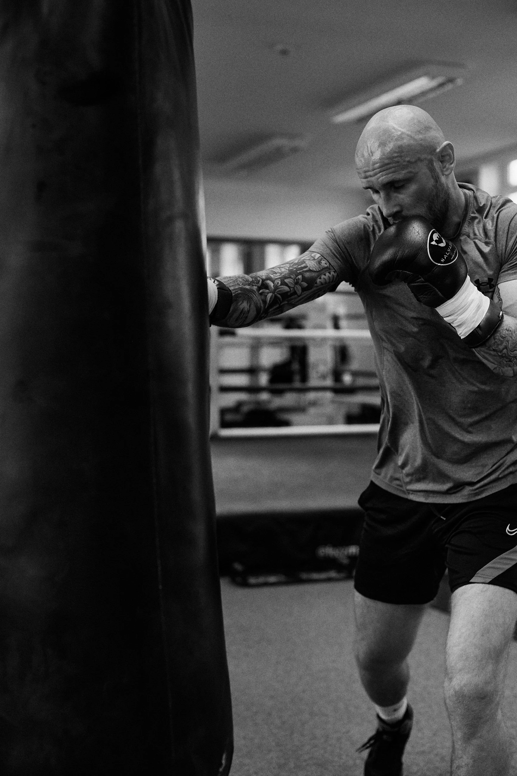 A man with tattoos on his arm is practicing boxing with a punching bag in a gym.