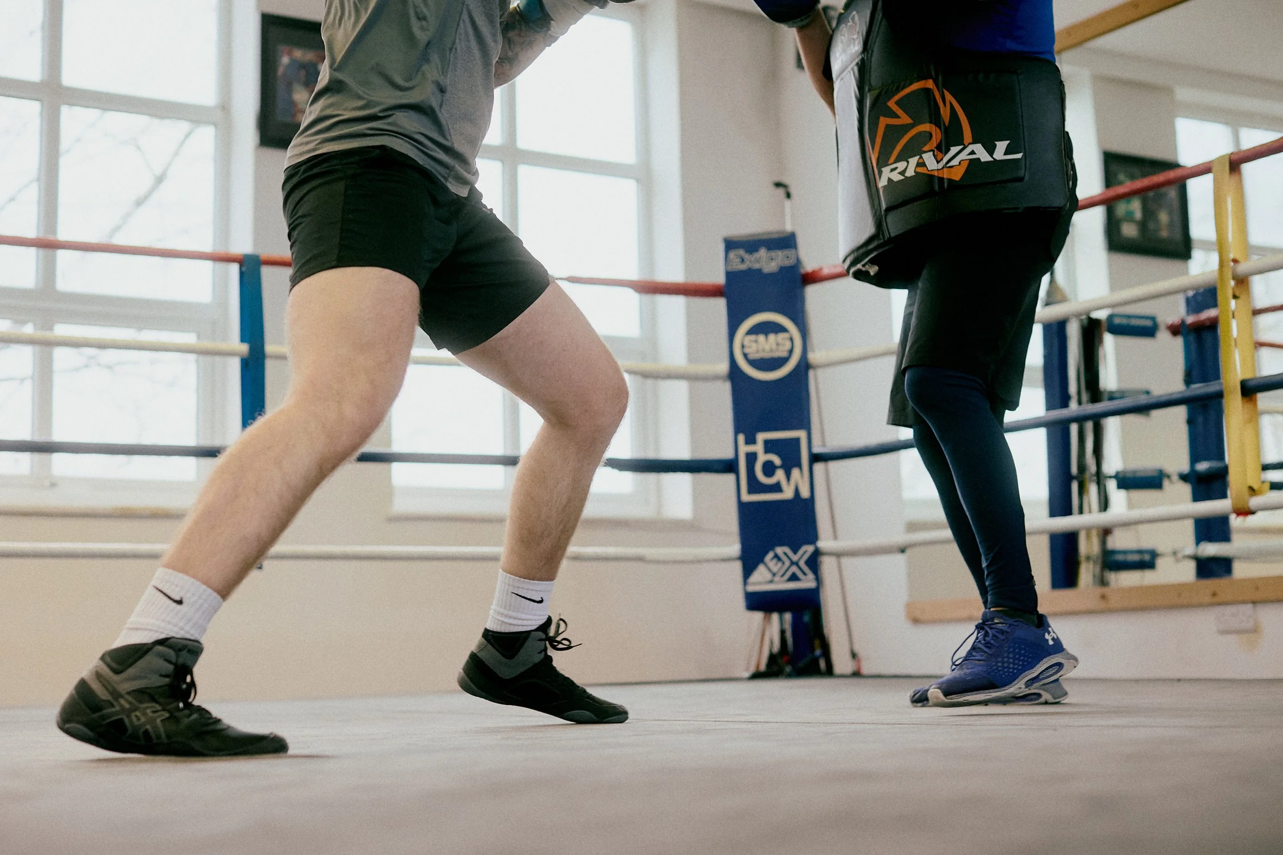 Boxer practicing in the boxing ring with a trainer carrying a towel in a gym.