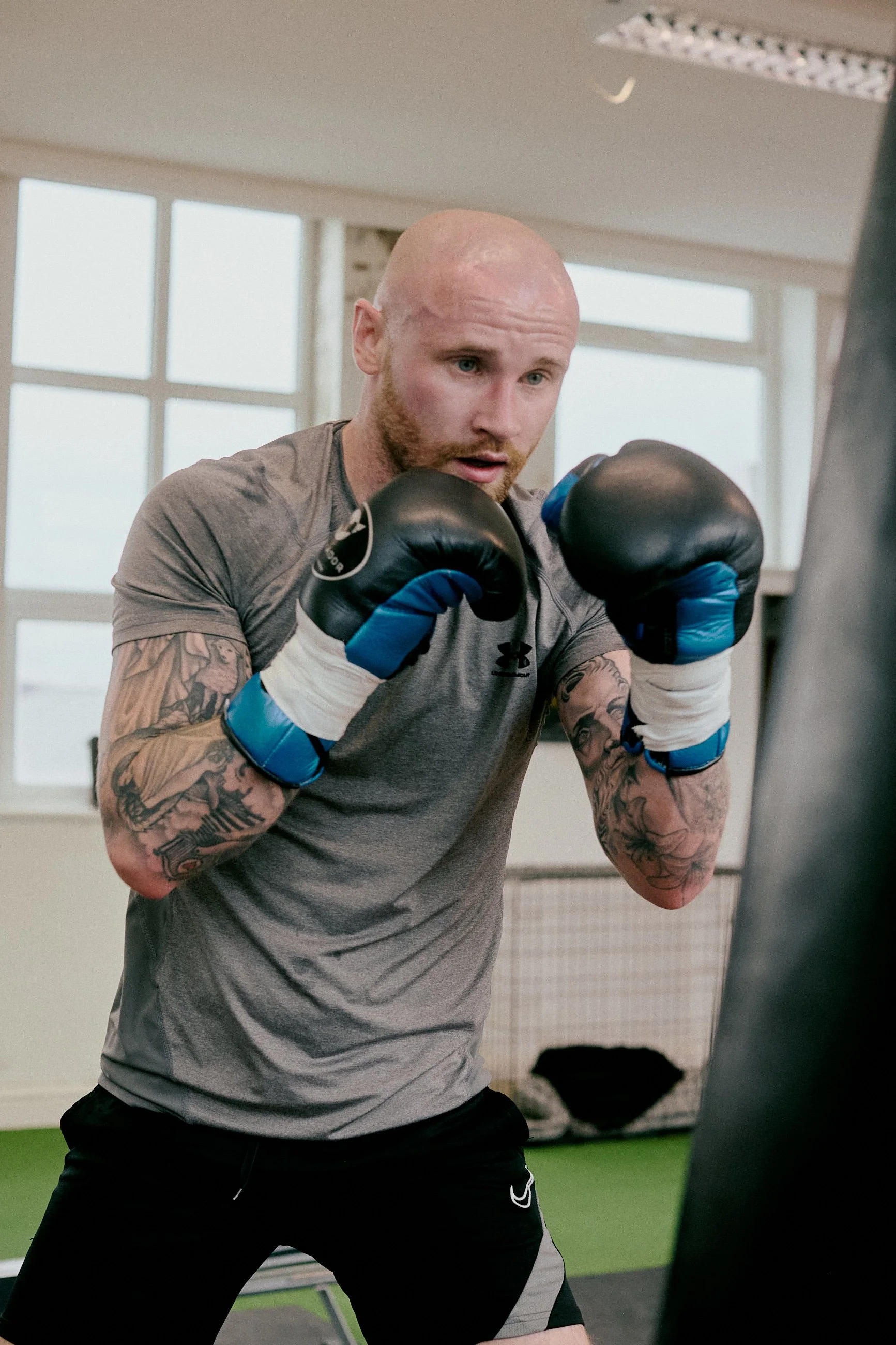 Man with tattoos and boxing gloves practicing boxing in a gym.