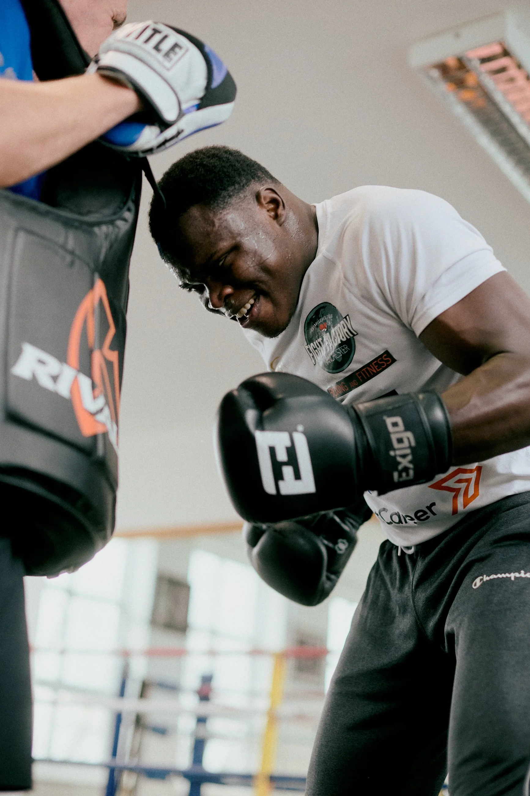 A young man in boxing gloves practicing punches on a punching bag in a gym, showing effort and focus.