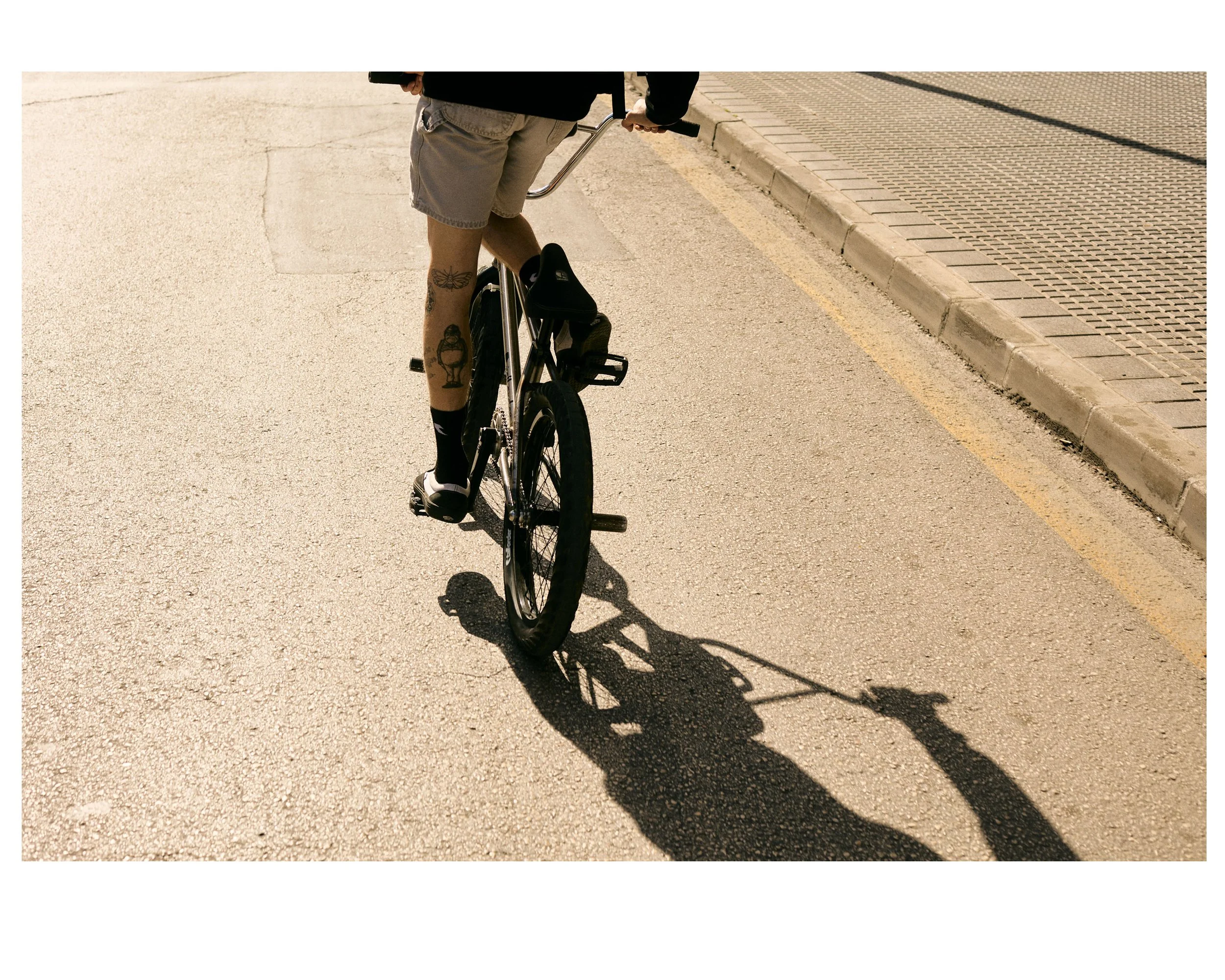 Person riding a bicycle on a sunny street with their shadow cast on the ground.