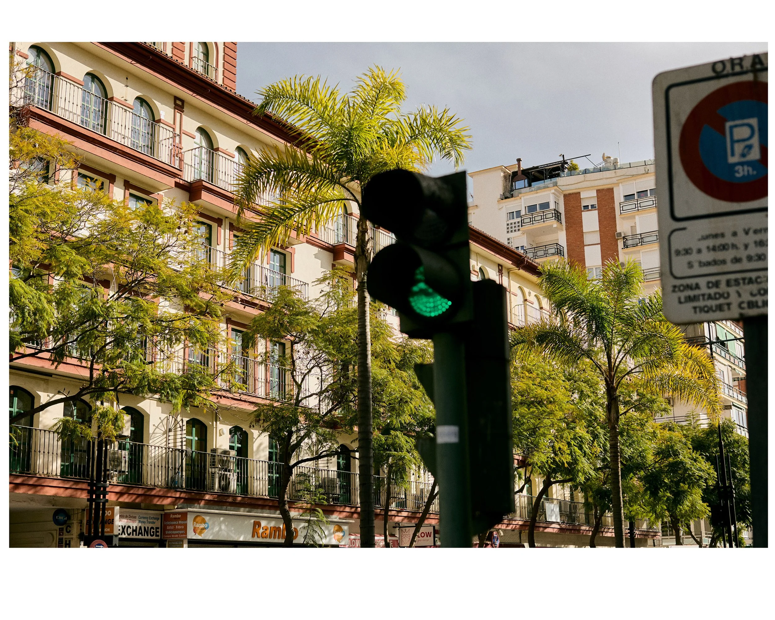City street scene with a traffic light showing green, surrounded by trees and high-rise residential buildings in the background.