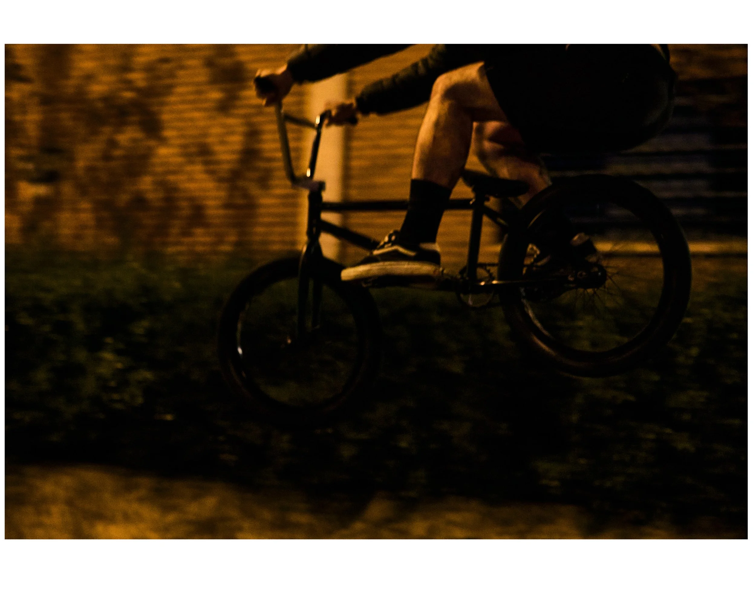 A person riding a bicycle at night against a brick wall, with dark surroundings and low lighting.