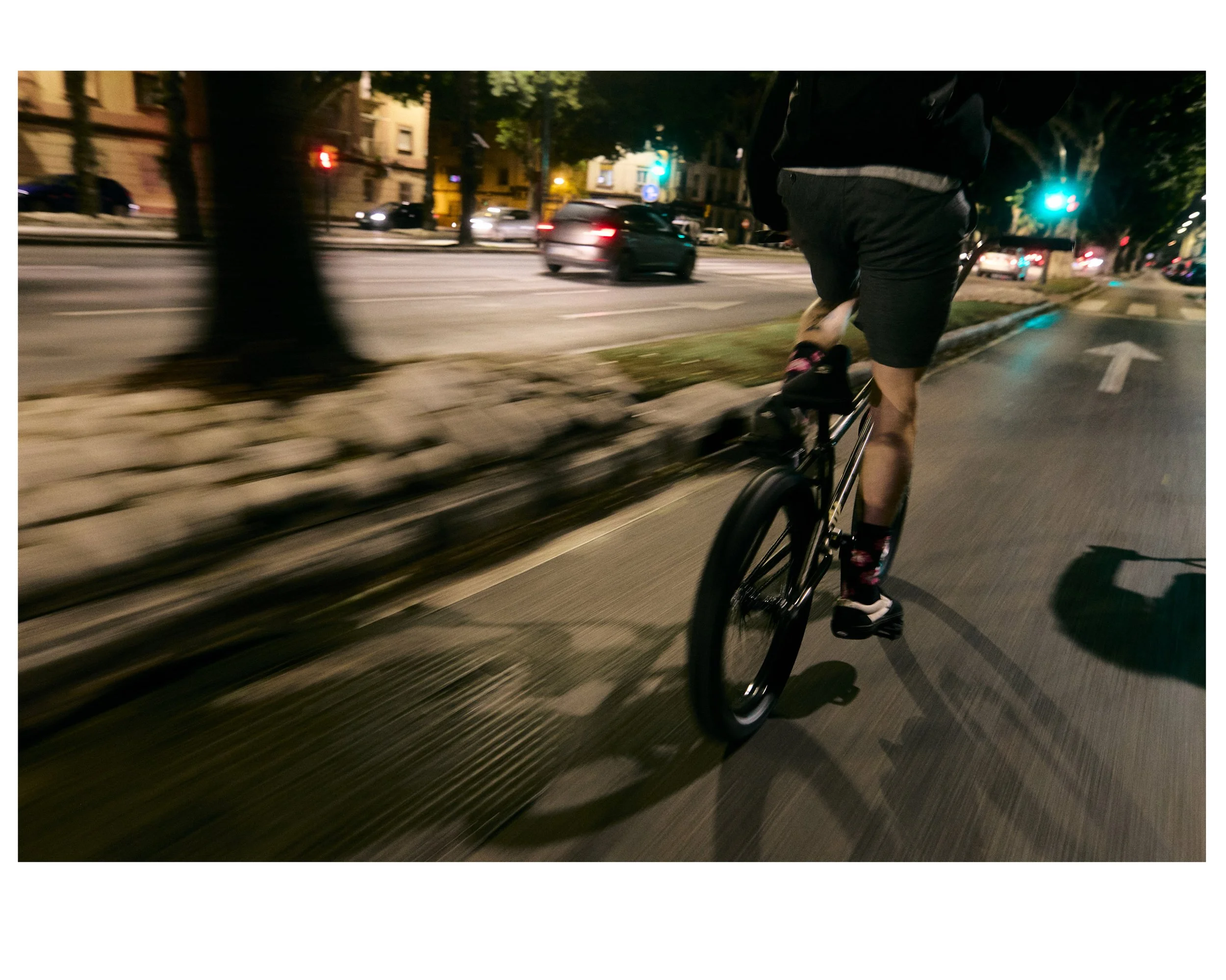A person riding a bicycle on a city street at night, with cars and buildings in the background.