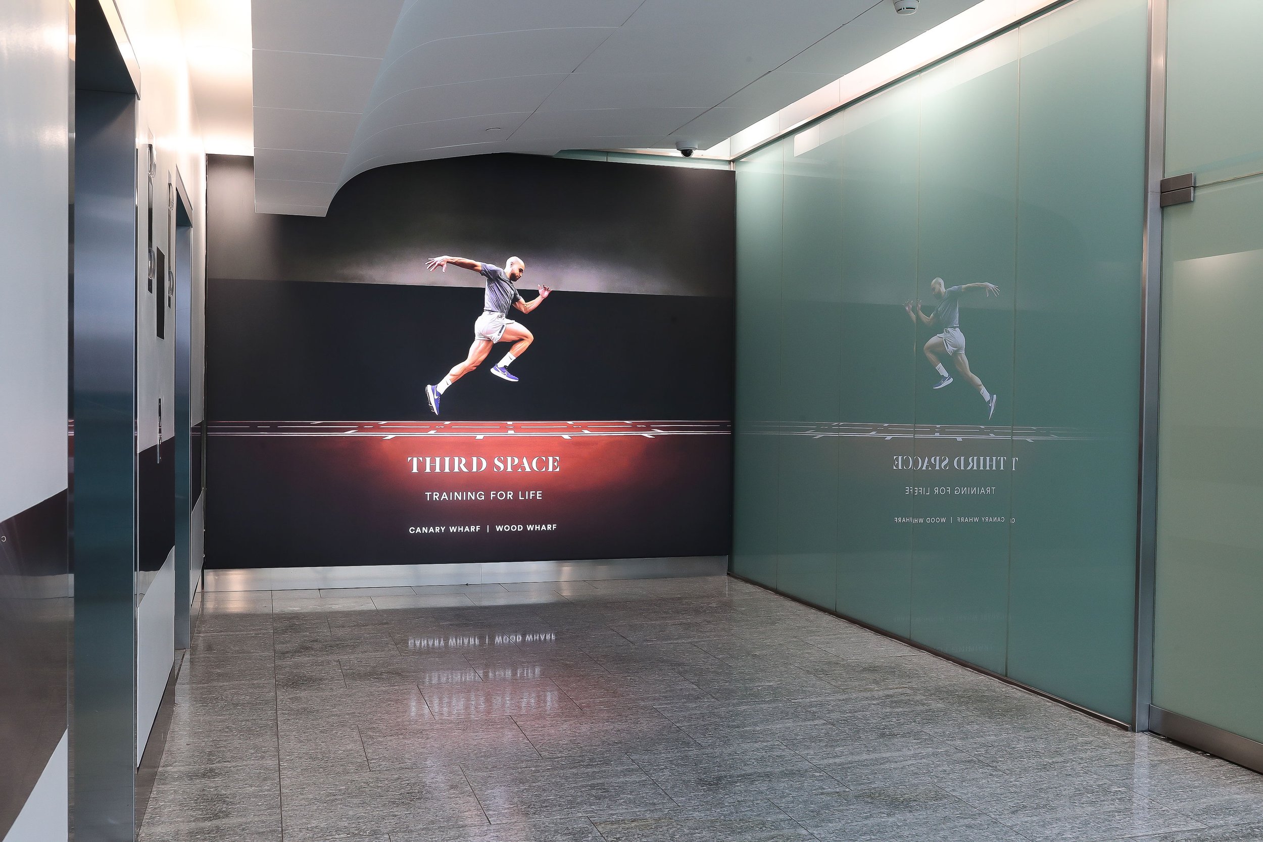 Advertisement for Third Space gym featuring a man in mid-air while running on a track, with the text 'Third Space, Training for Life, Canary Wharf, Wood Wharf'.