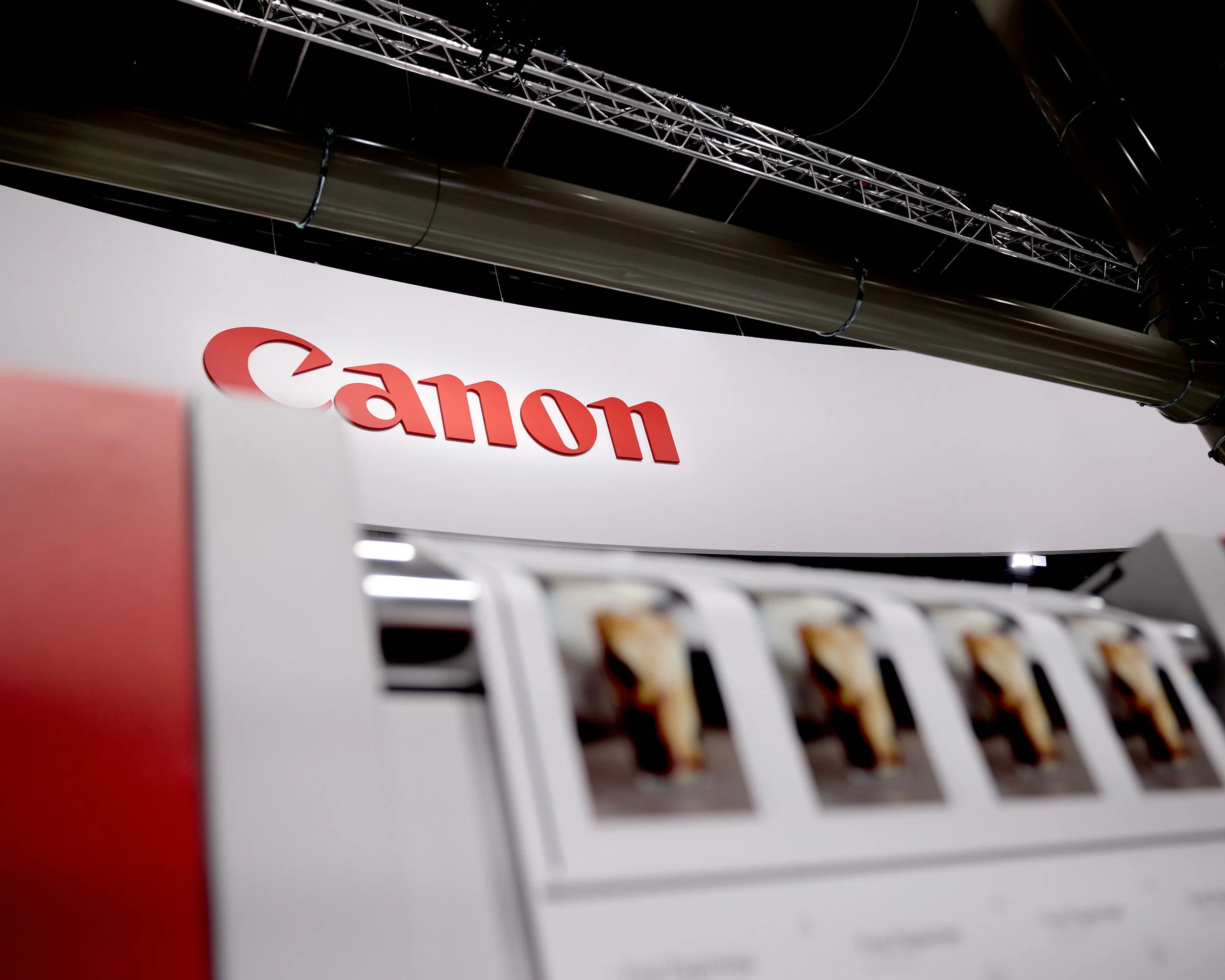 Close-up of a Canon logo on a white wall with a blurred machine in the foreground.