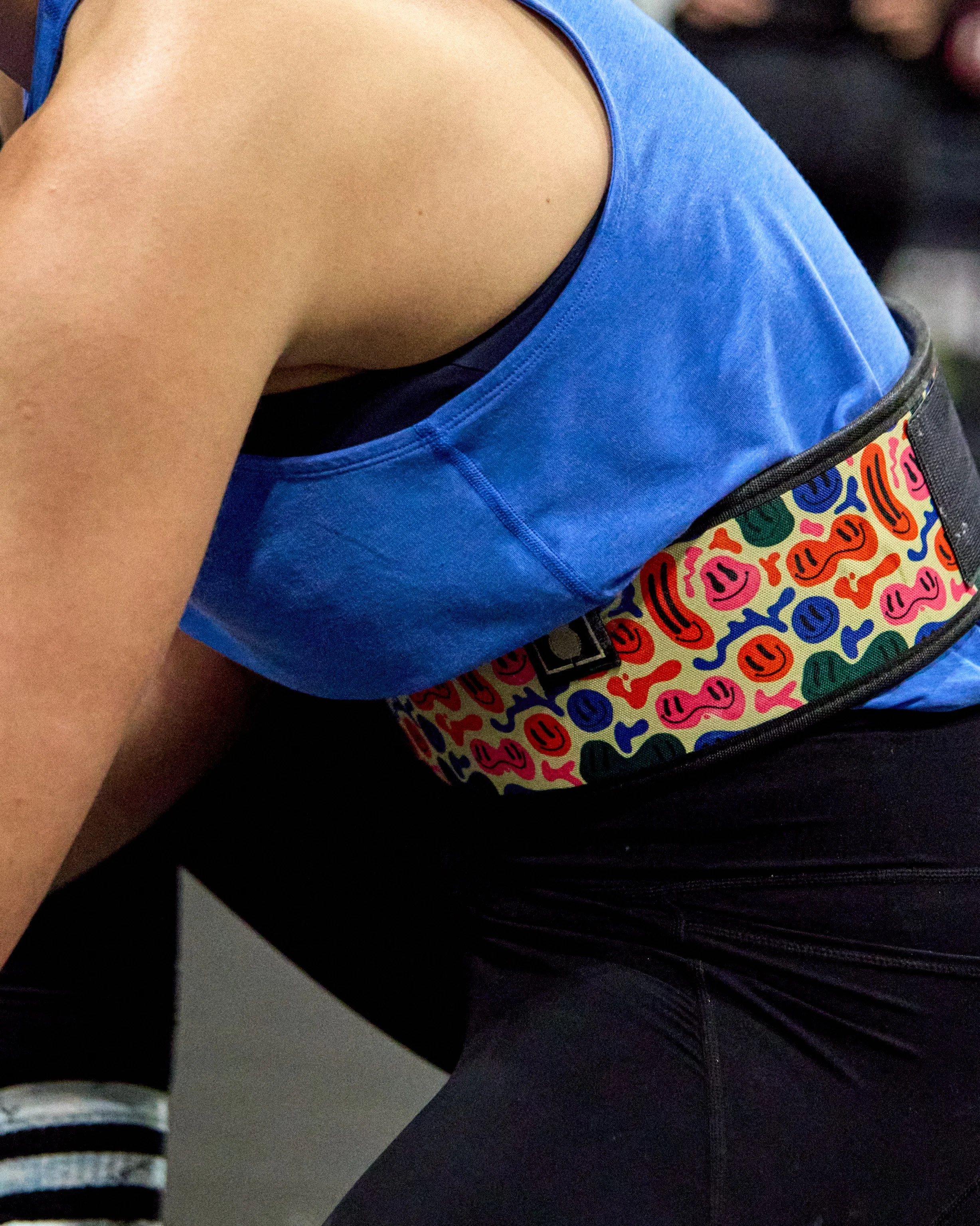 Close-up of a person wearing a blue tank top, black leggings, and a colorful waist bag with smiley face patterns.