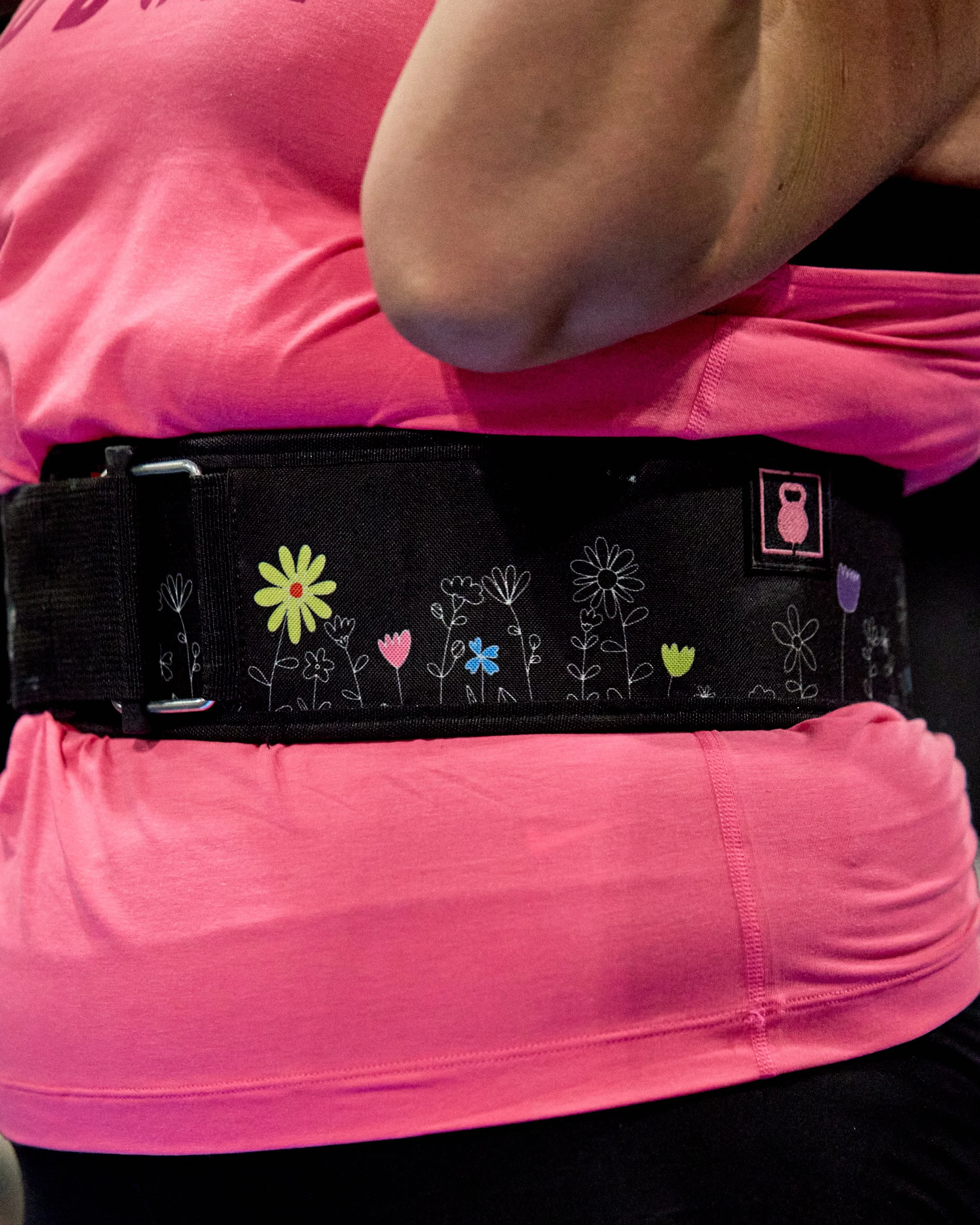 Close-up of a person wearing a pink shirt and a black belt with colorful flower and kettlebell designs.