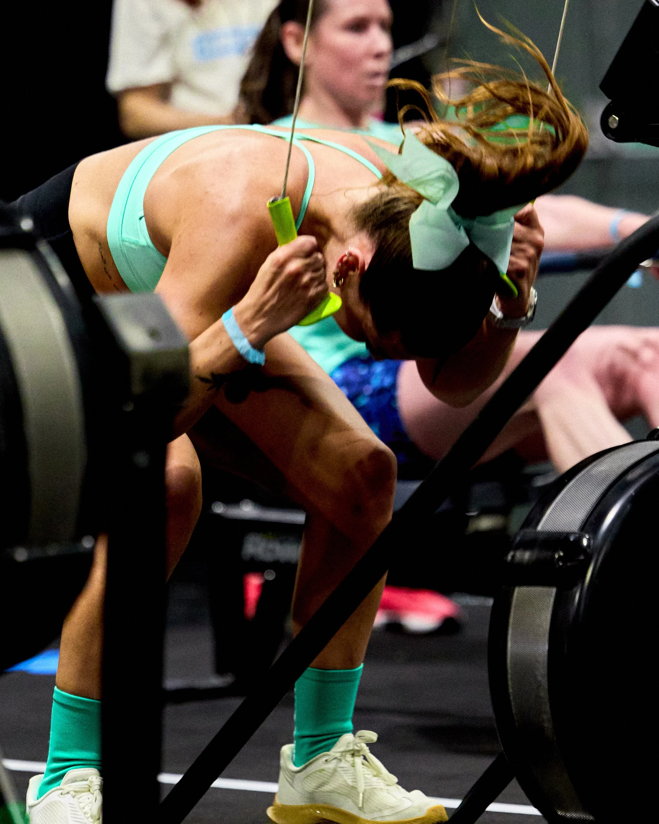 A woman in athletic clothing and a bow in her hair appears exhausted while using a treadmill in a gym, holding onto the machine's handles.