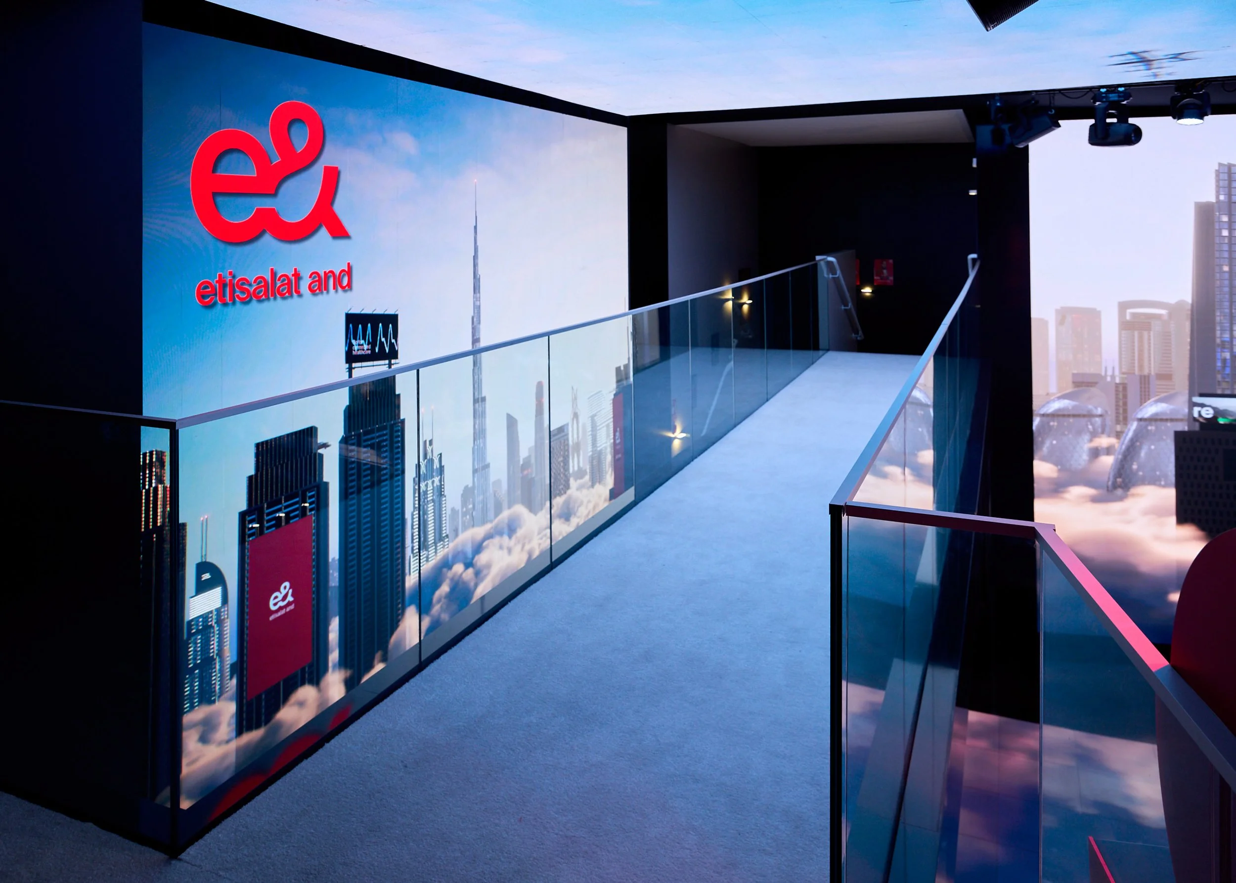 Interior of a modern building with a glass walkway, cityscape mural, and a large digital display featuring the Etisalat logo and Dubai skyline.