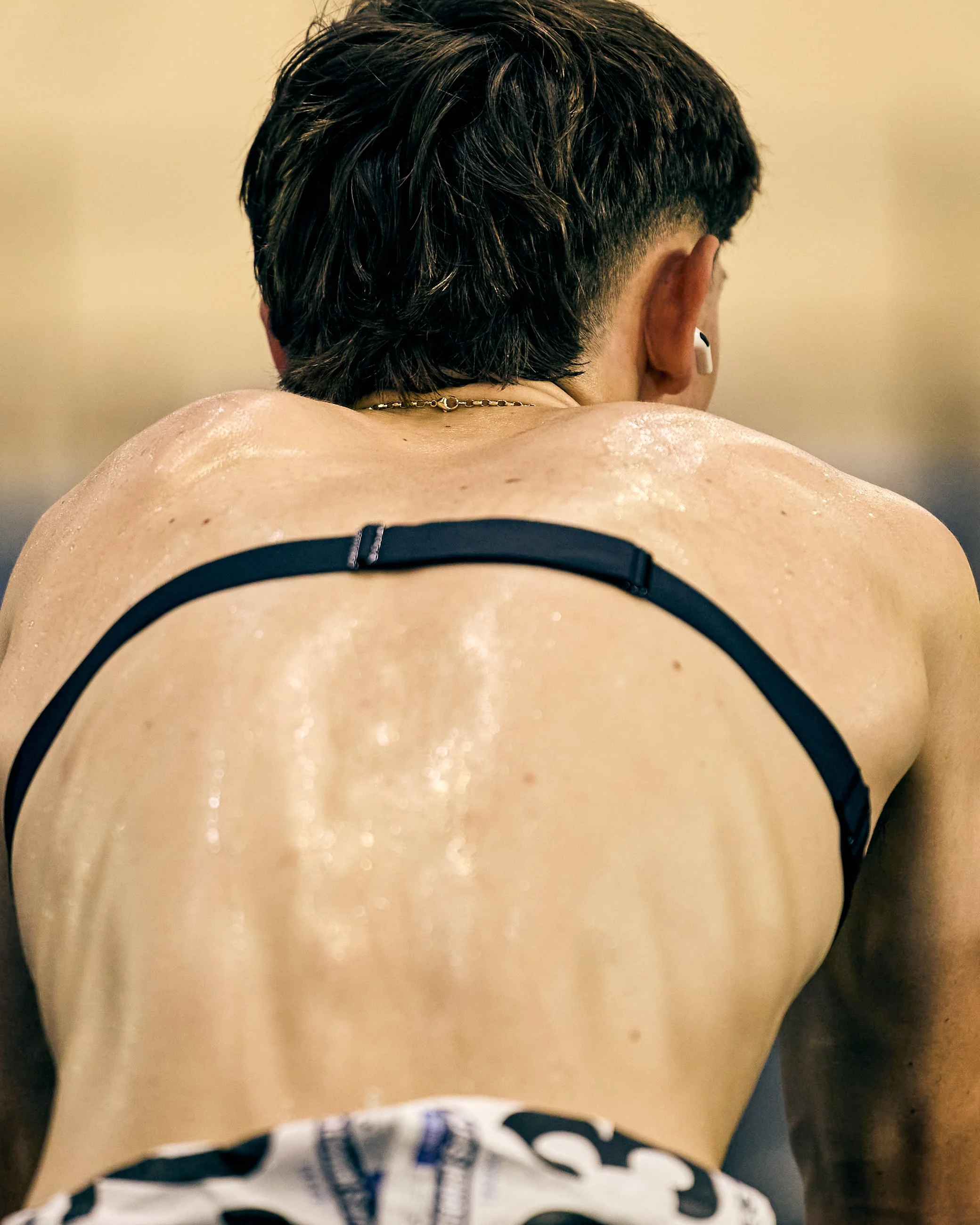 Back view of a person with wet hair, wearing a black sports bra and patterned shorts, showing sweat on their back.