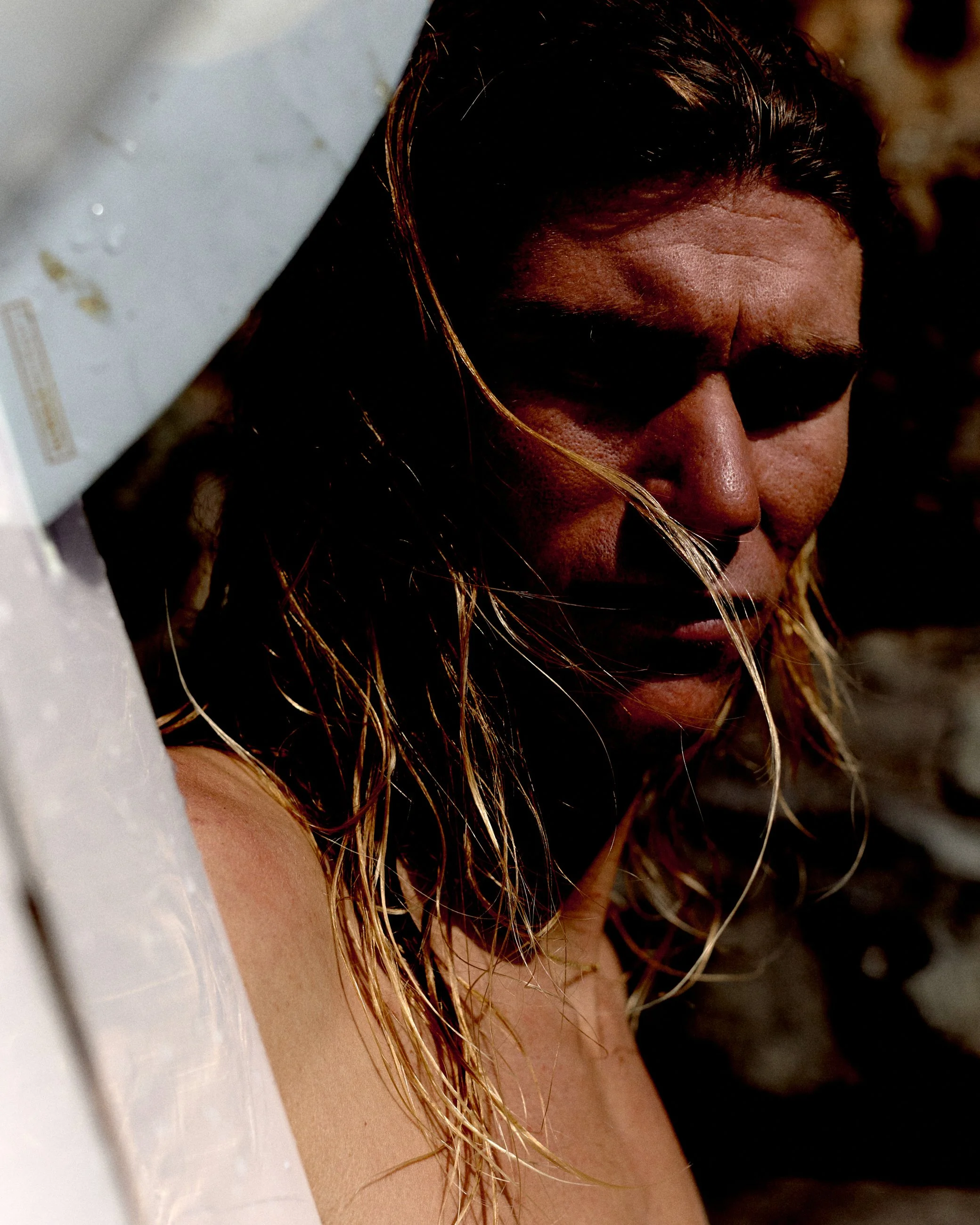 Close-up of a woman with long, wet hair, looking down, with a shadowed face, blurred background.