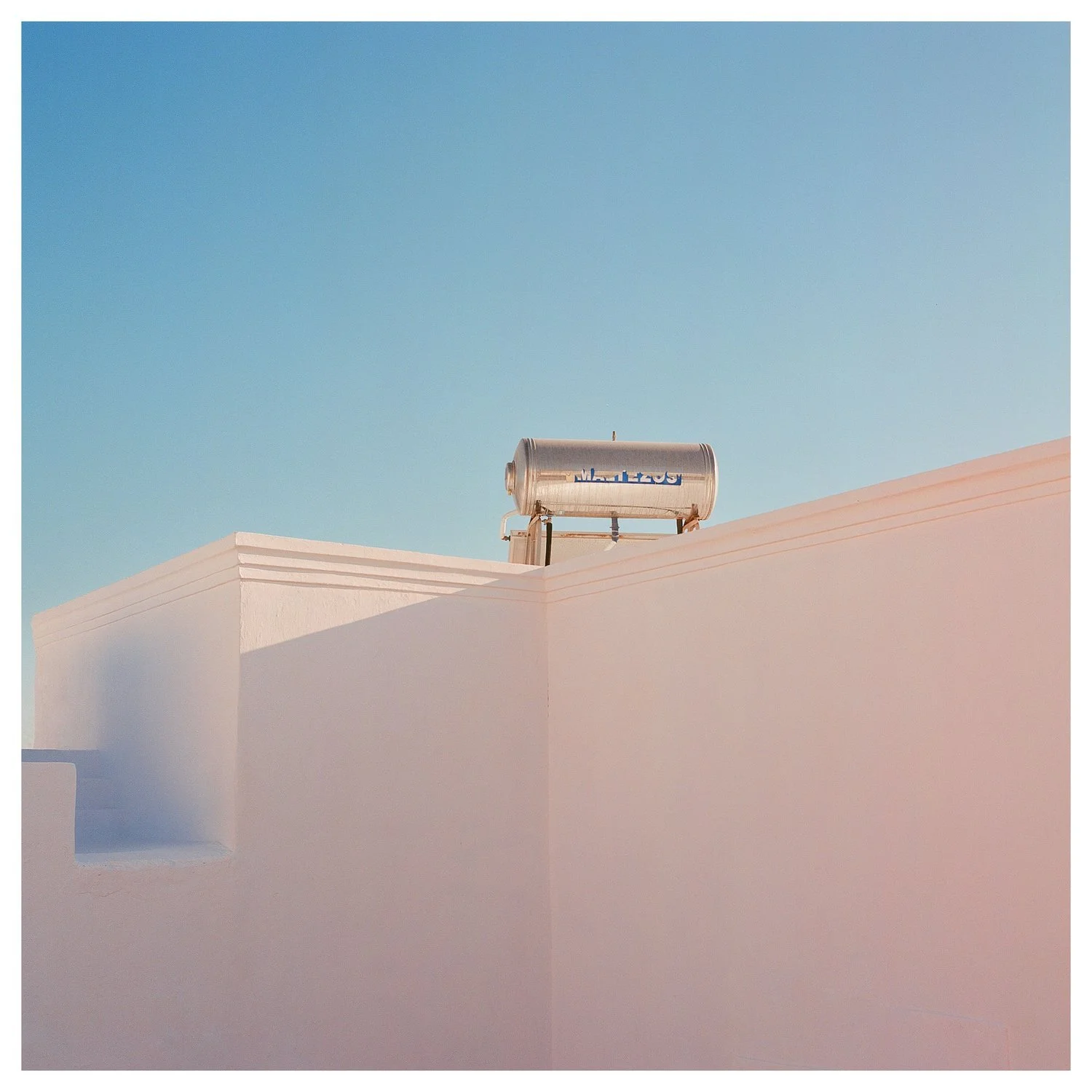 A white building with a blue sky background and a cylindrical metallic water heater mounted on the roof.