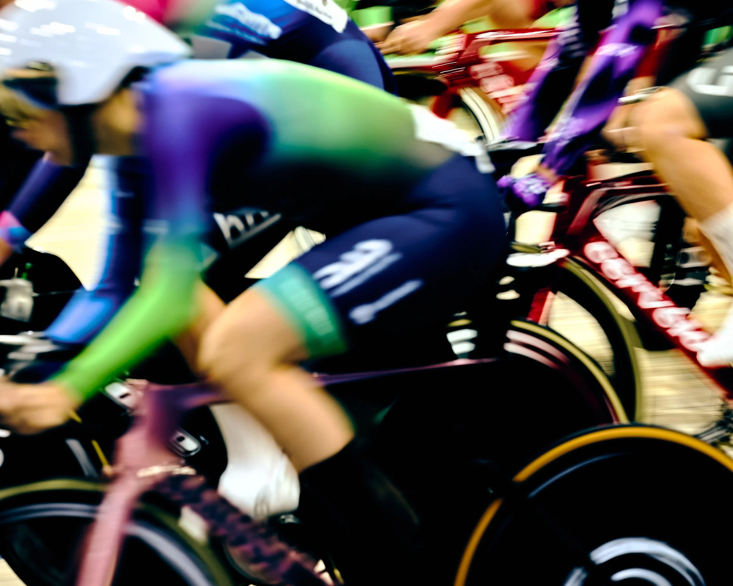 Close-up of a group of cyclists racing, with focus on their colorful cycling uniforms and bikes, capturing a motion blur to convey speed.