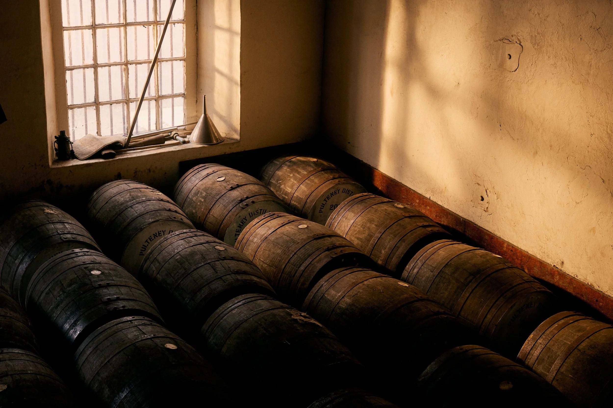 Several wooden barrels in a dimly lit room near a window with sunlight streaming in.