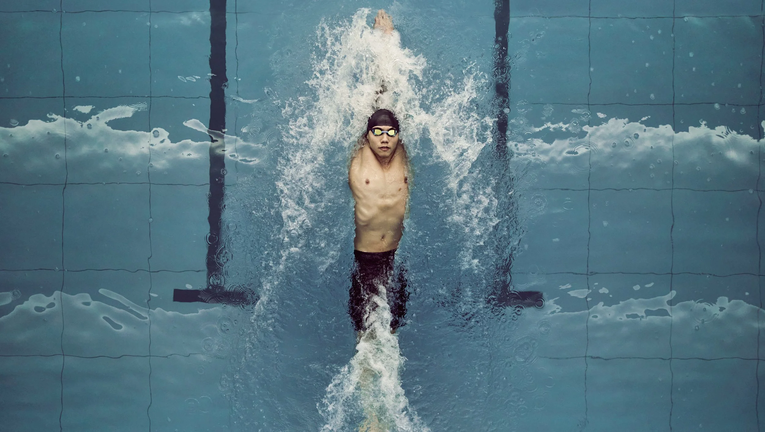 Swimmer in black swim trunks and goggles performing a backstroke in a pool with lane markers.