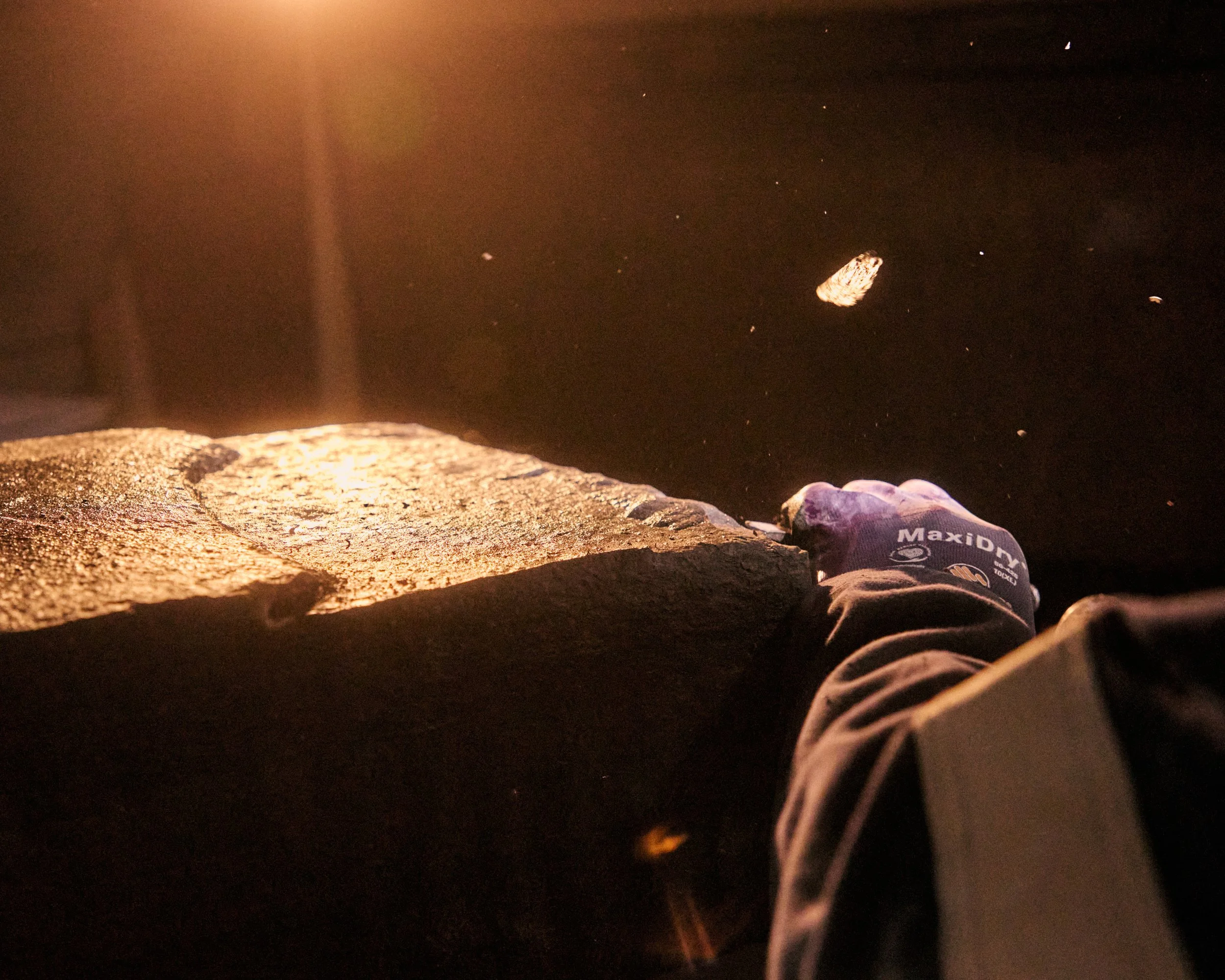 An individual wearing a MaxID glove reaching up to move a large rock or boulder at night, illuminated by warm orange light.