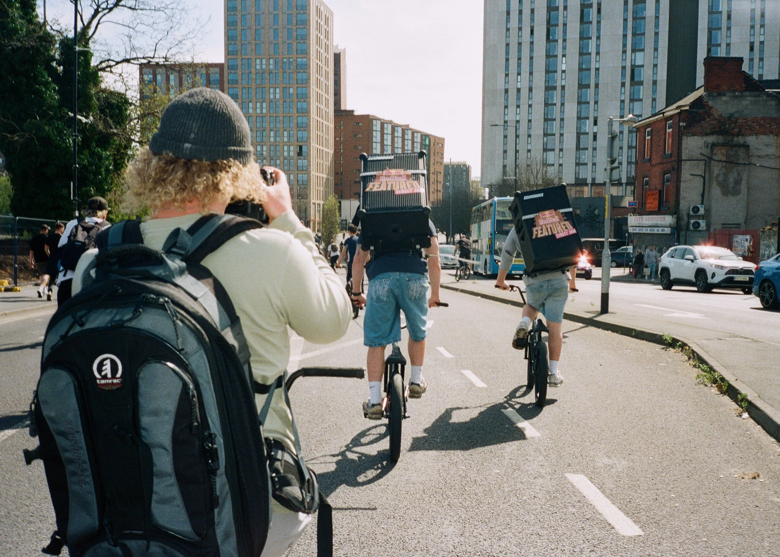 People riding bicycles on a city street with tall buildings, cars, and a bus in the background.