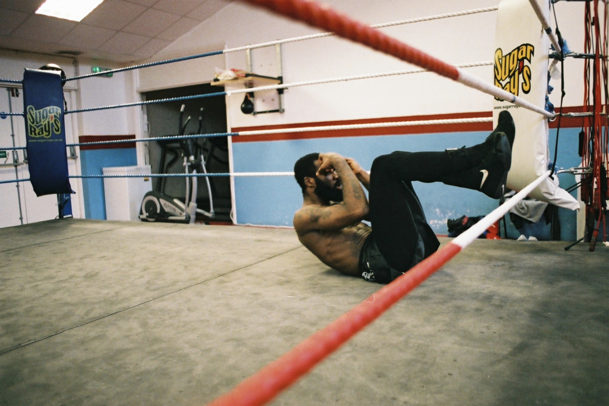 A man practicing sit-ups in a boxing gym, lying on the mat inside a boxing ring.