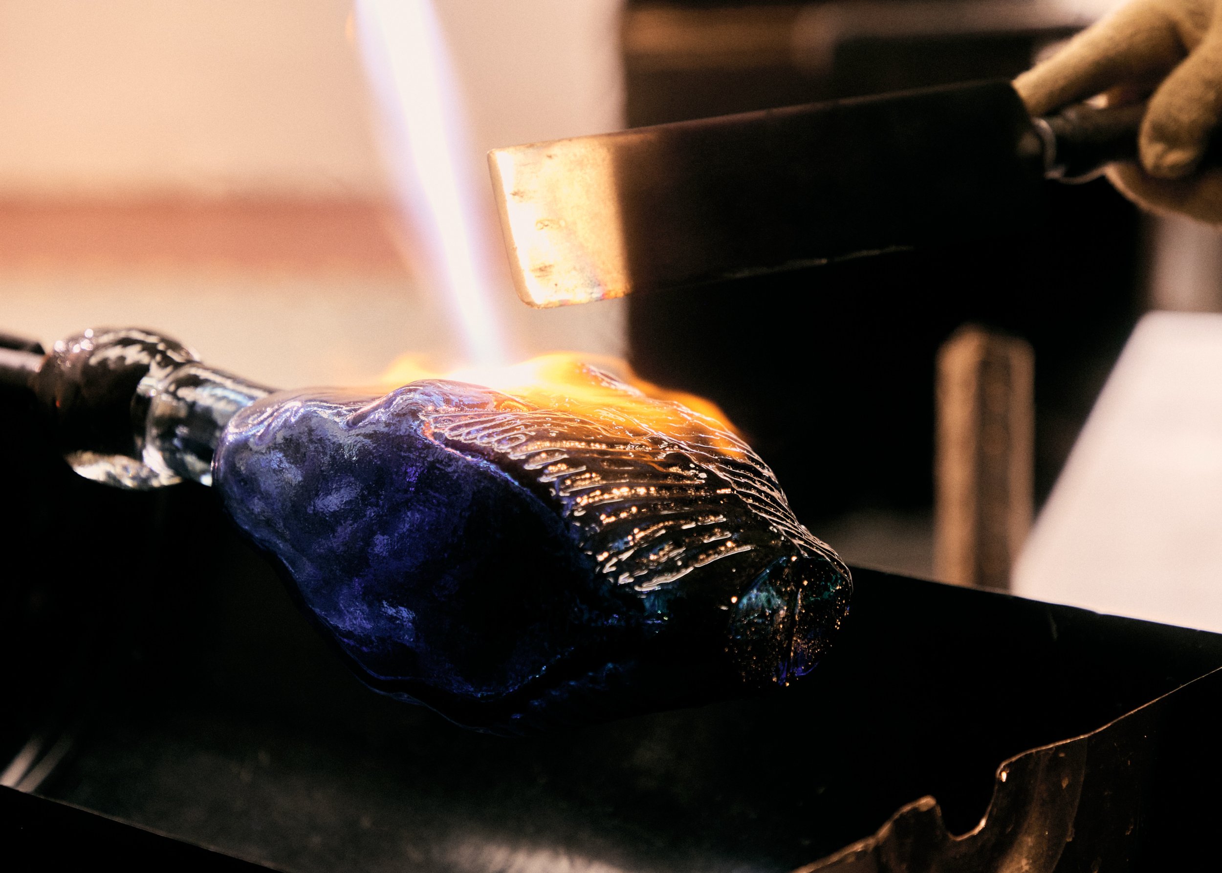 A glassblower shaping a glowing piece of molten glass over an open flame.