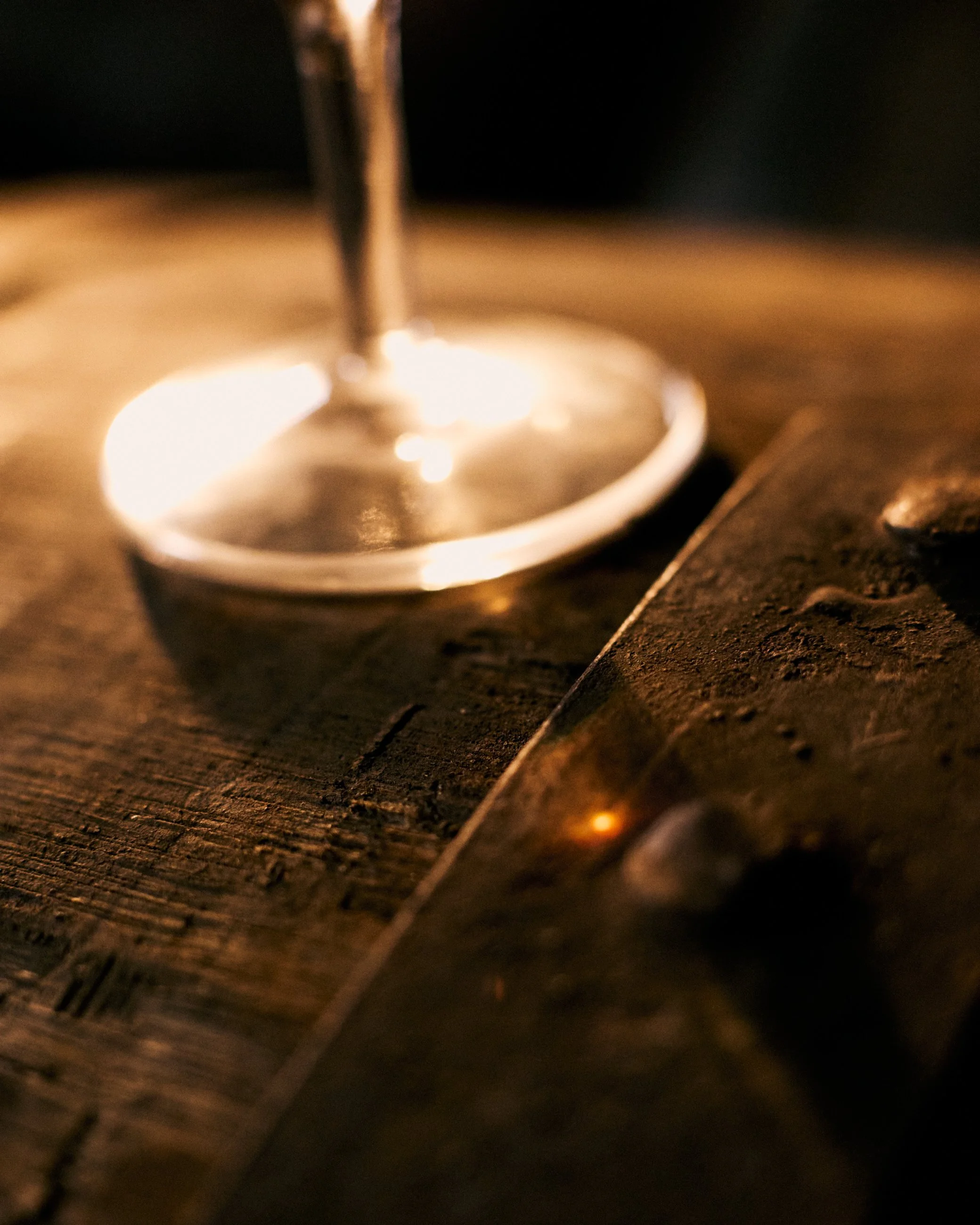 Close-up of the base of a wine glass on a wooden table with a warm, dim light.