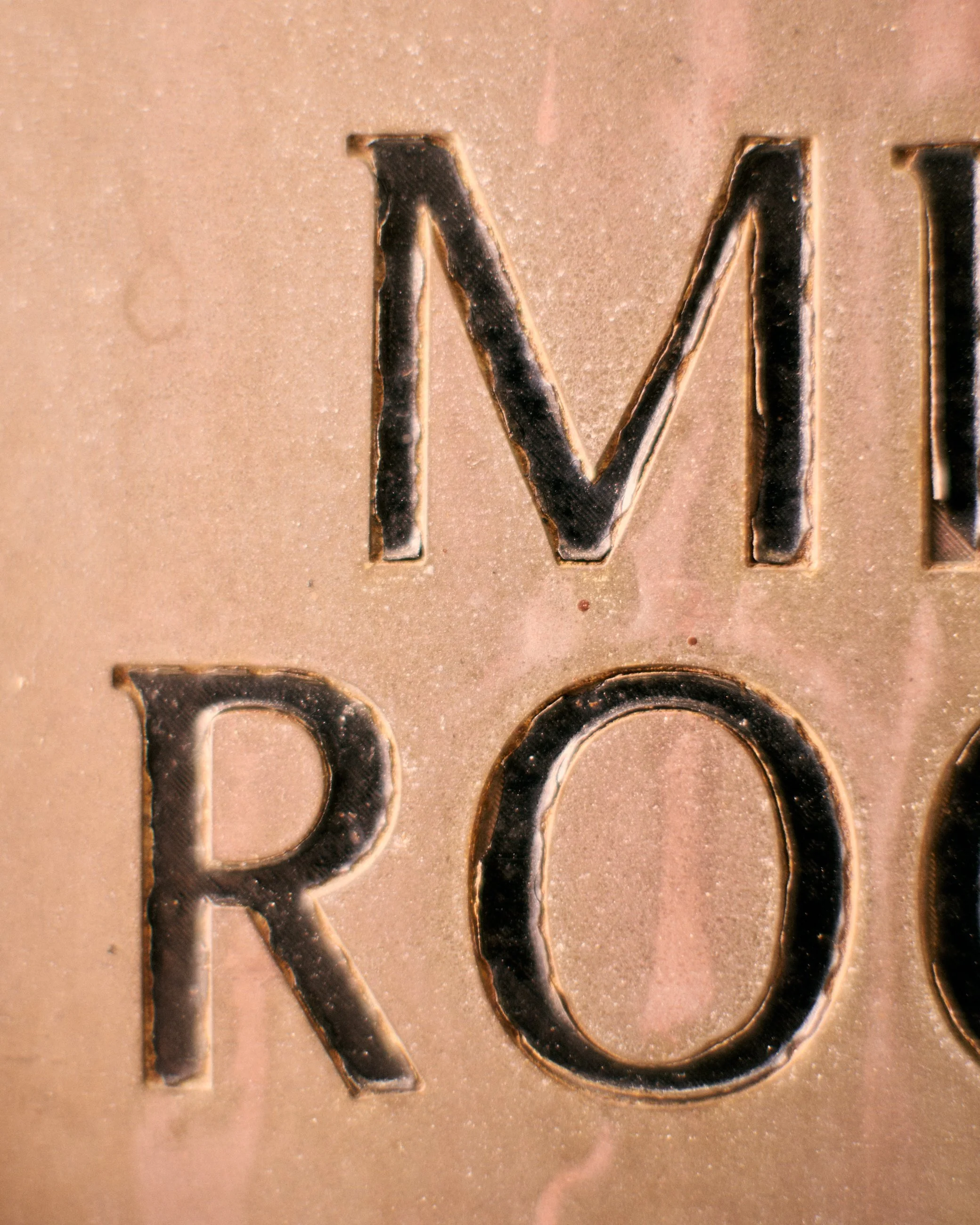 Close-up of embossed metallic letters on a surface, showing the letter M and part of the letter R.