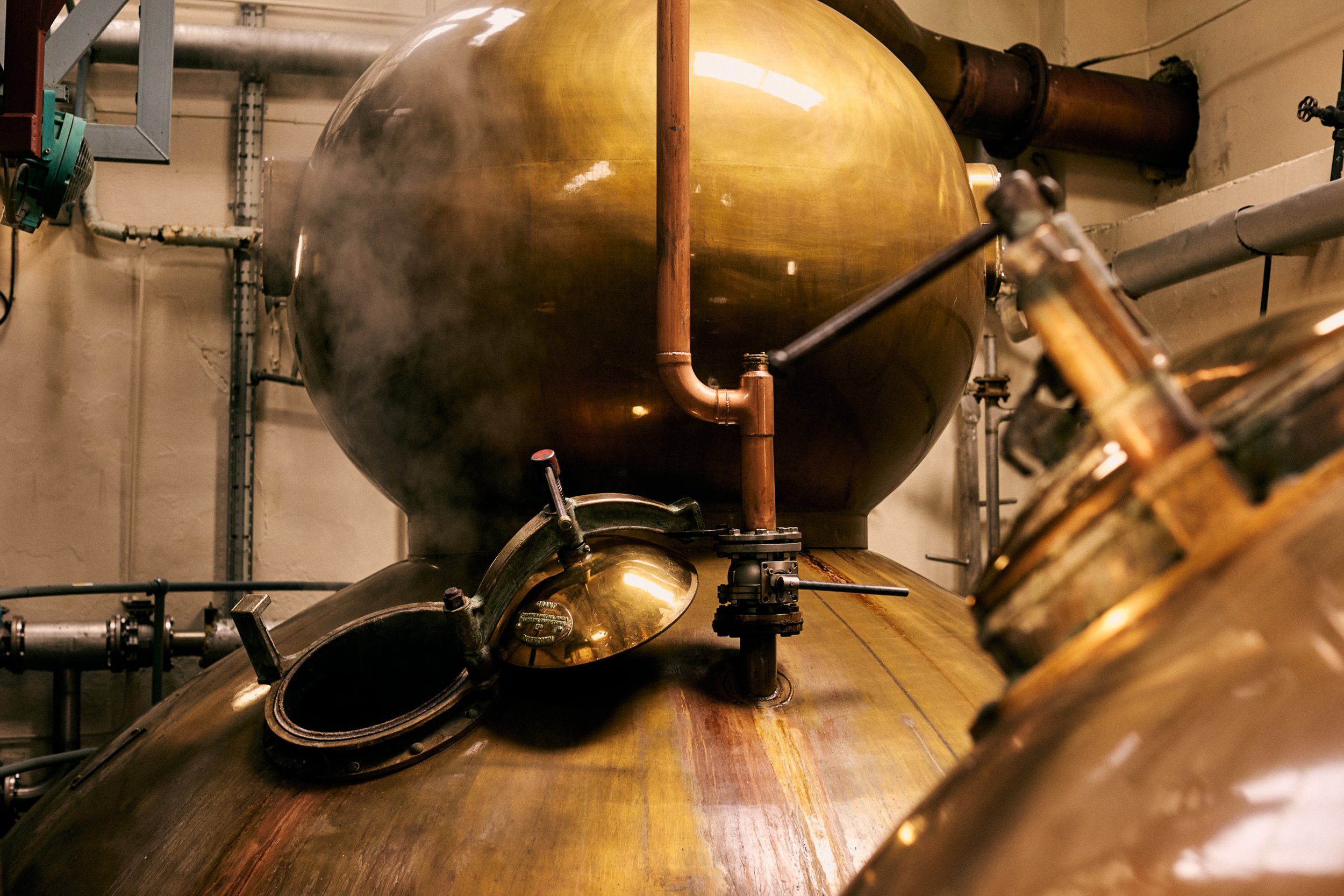 Close-up of a large copper still with steam rising from it in an industrial setting.